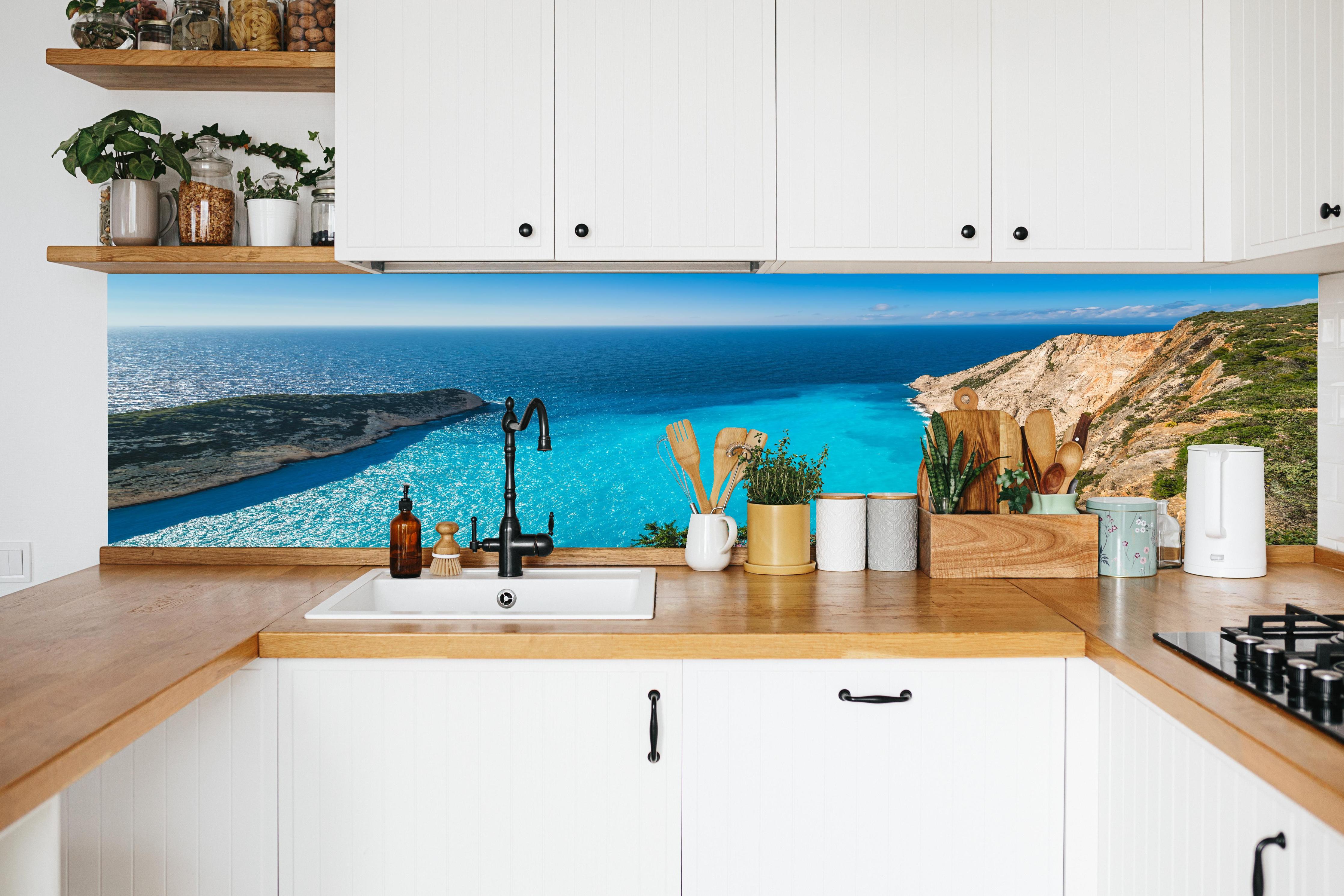 Küche - Atemberaubende Aussicht auf türkisblaue Küstenlandschaft hinter weißen Hochglanz-Küchenregalen und schwarzem Wasserhahn