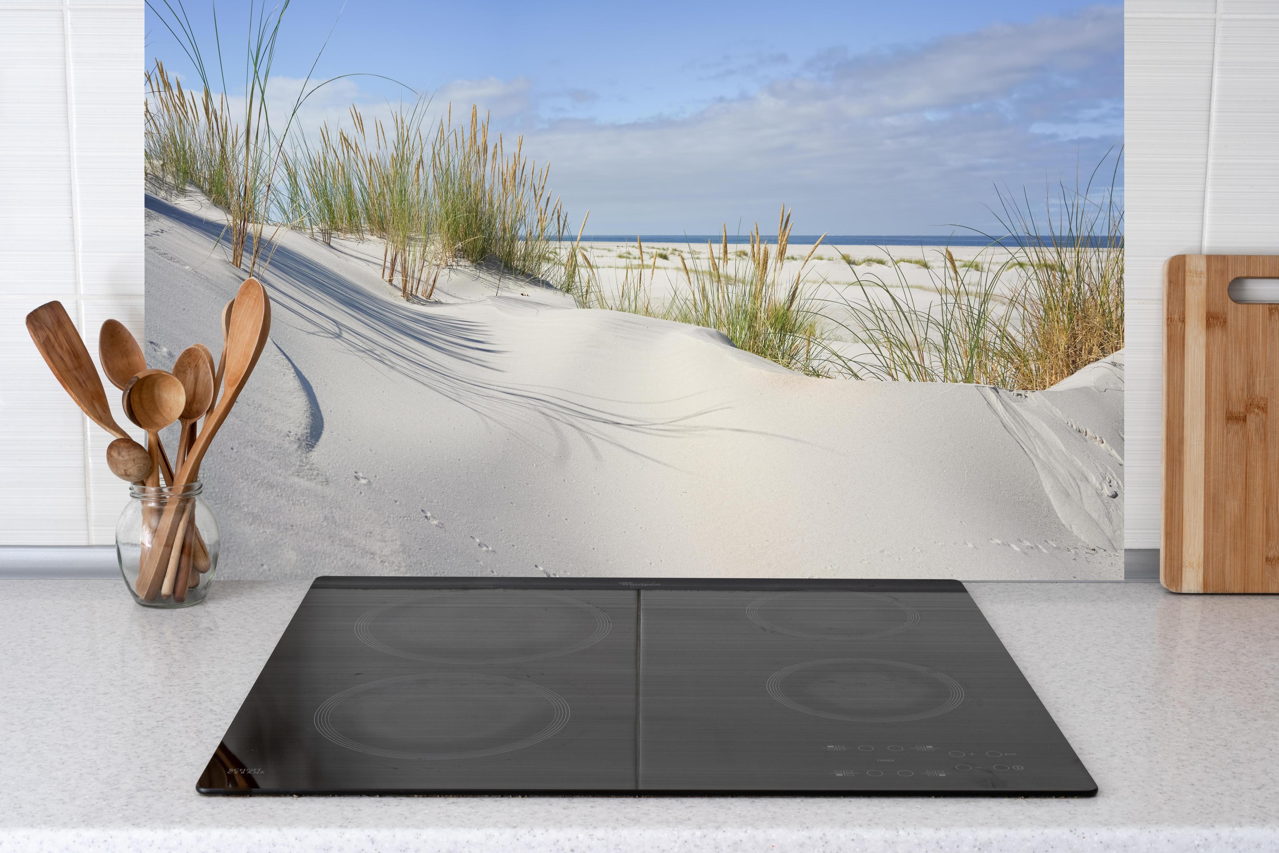 Küche - Beruhigende weiße Dünenlandschaft mit sanften Gräsern am Ozean hinter weißen Hochglanz-Küchenregalen und schwarzem Wasserhahn