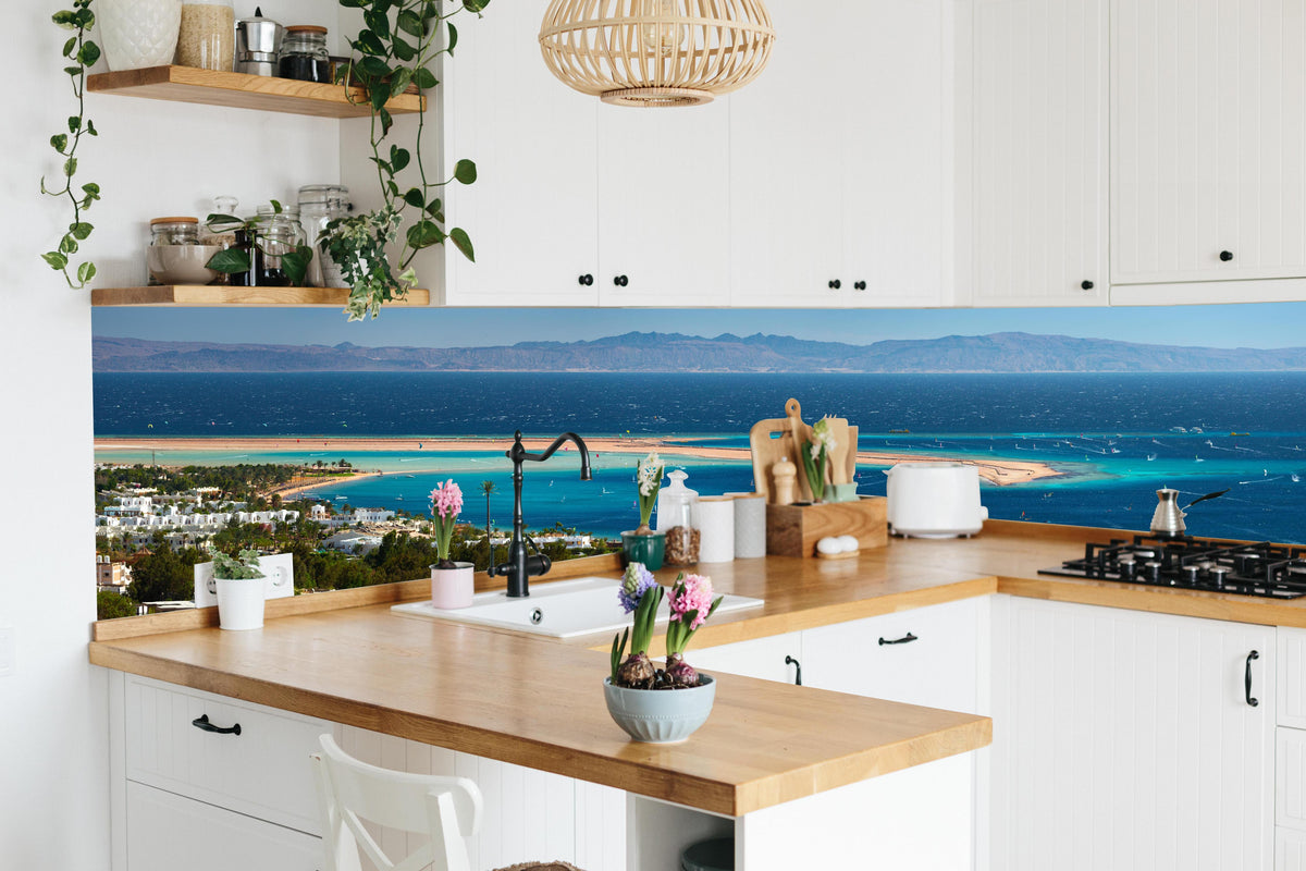 Küche - Blaue Lagune am Meer Panoramabild hinter weißen Hochglanz-Küchenregalen und schwarzem Wasserhahn