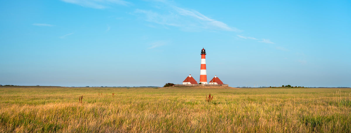 Küchenrückwand-Ein beeindruckender Leuchtturm in der weitläufigen norddeutschen Landschaft unter blauem Himmel.