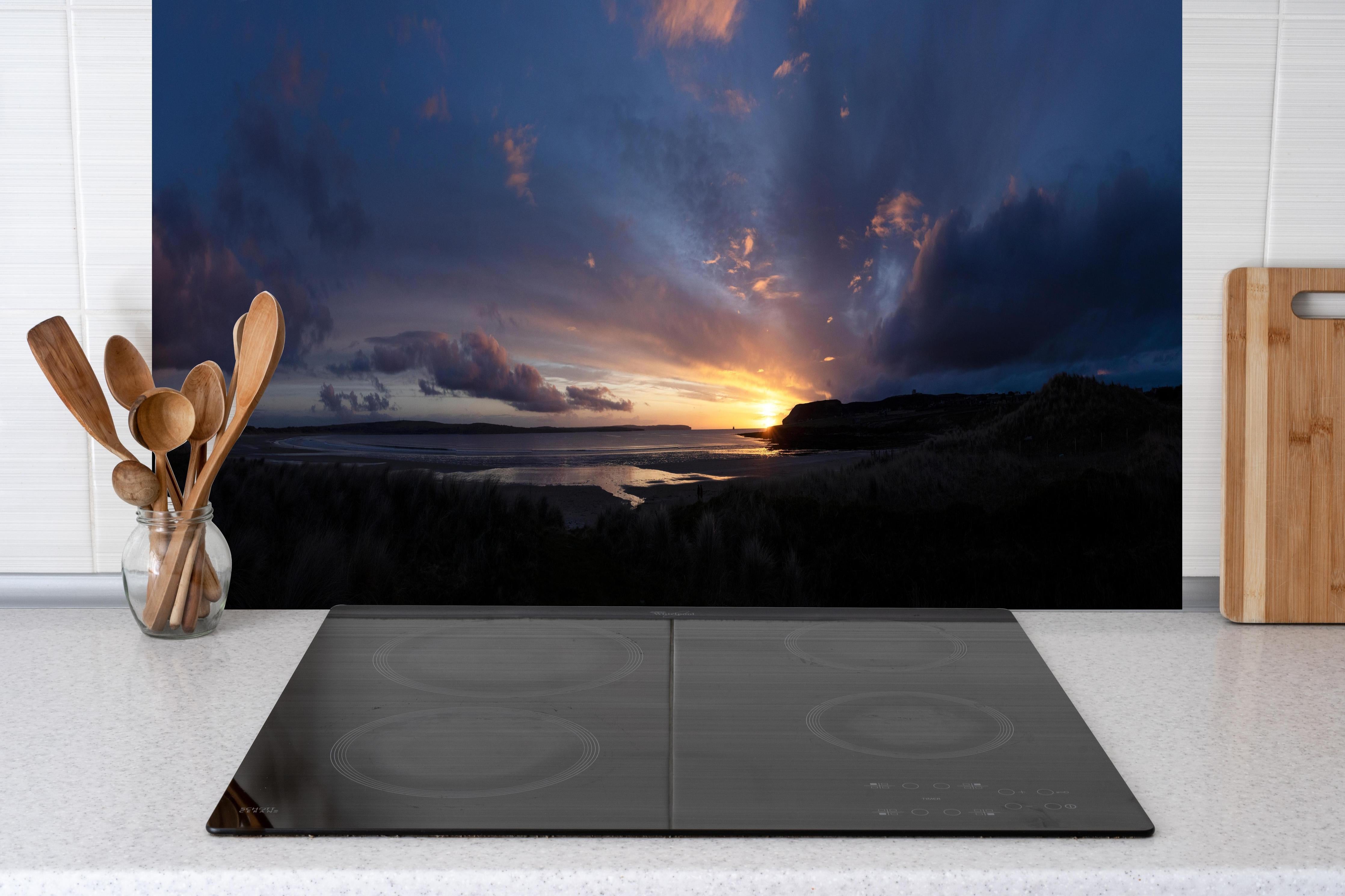 Küche - Ein malerischer Sonnenuntergang über einem ruhigen See, die Wolken leuchten in verschiedenen Blau- und Orangetönen hinter weißen Hochglanz-Küchenregalen und schwarzem Wasserhahn