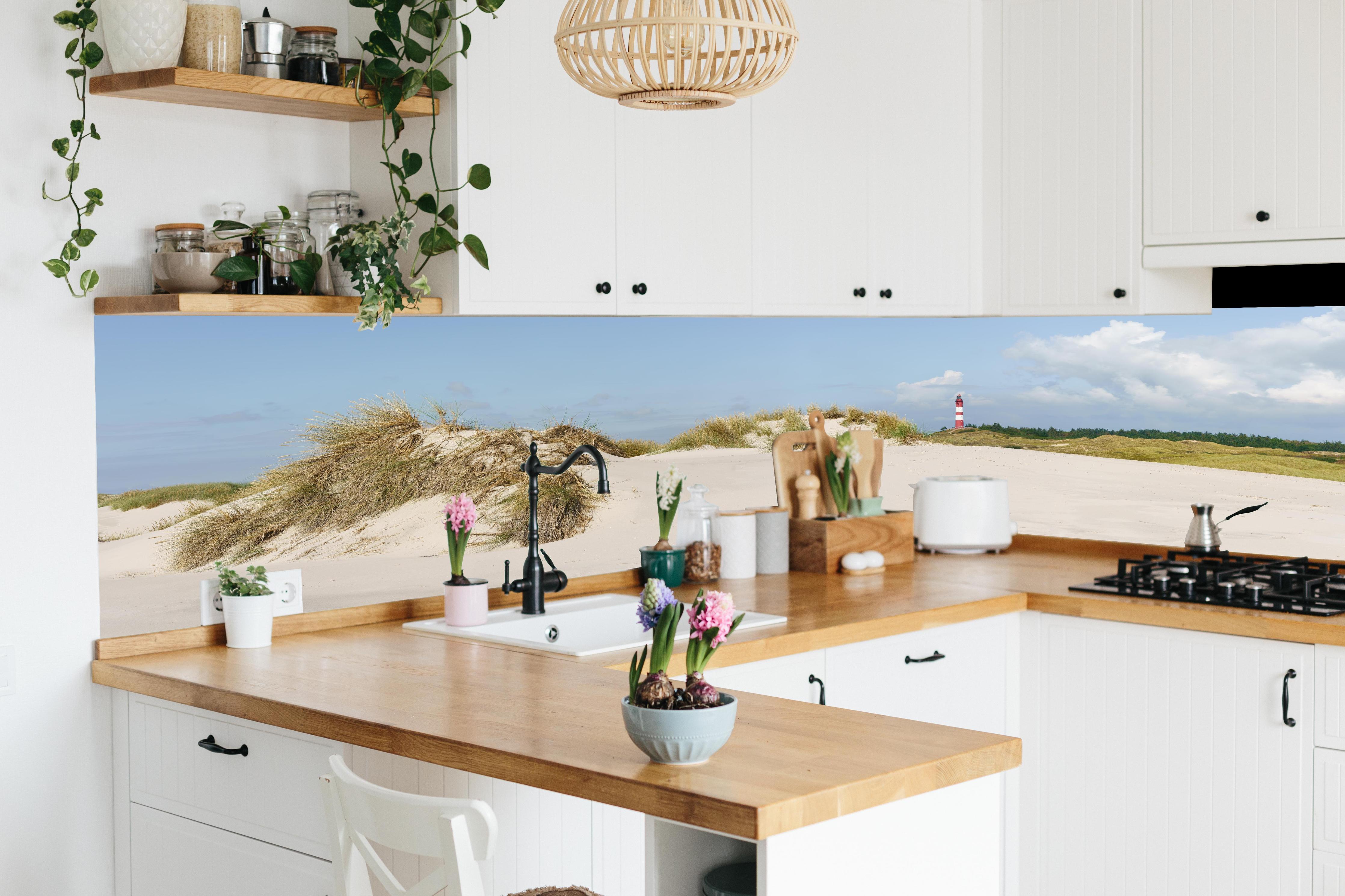Küche - Ein traumhafter Blick auf die weiße Sanddüne und den roten Leuchtturm am Meer hinter weißen Hochglanz-Küchenregalen und schwarzem Wasserhahn