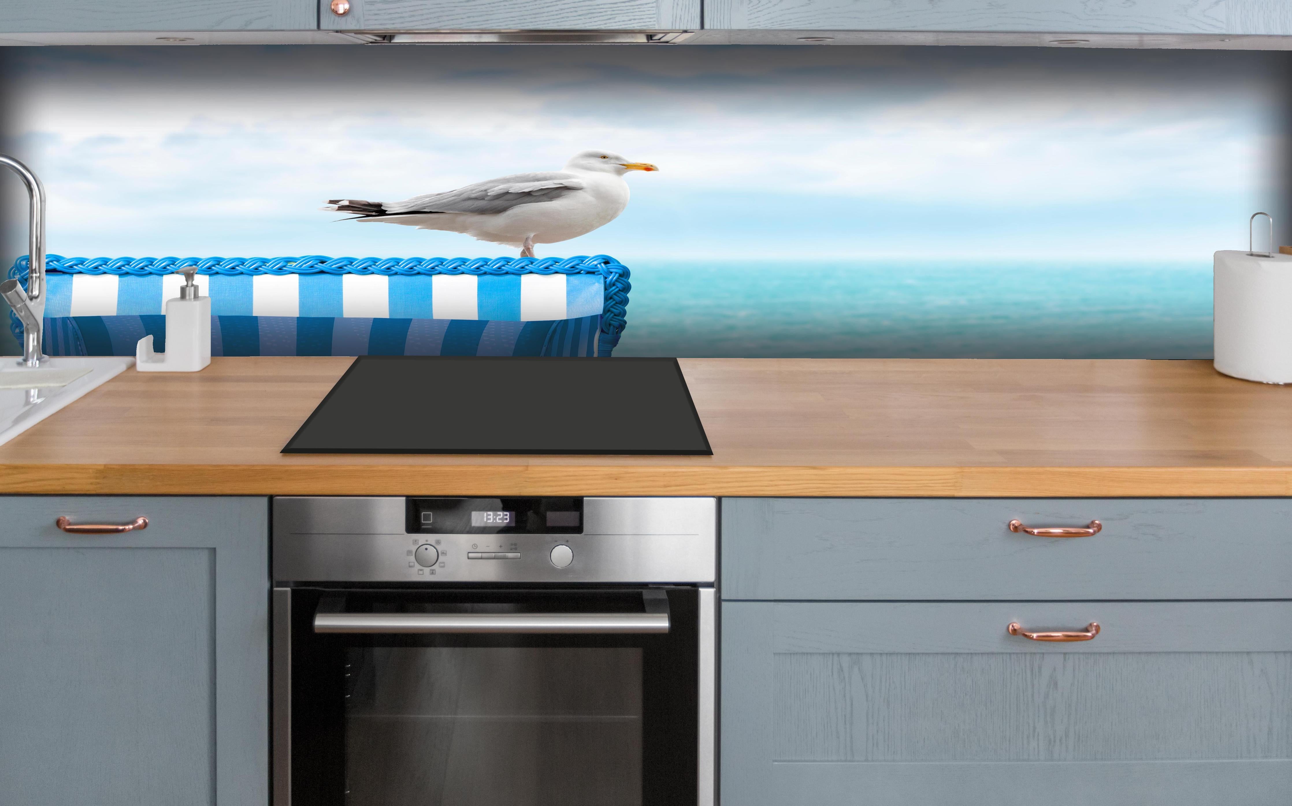 Küche - Elegant Seagull Perched on Blue Beach Chair by the Tranquil Ocean hinter weißen Hochglanz-Küchenregalen und schwarzem Wasserhahn