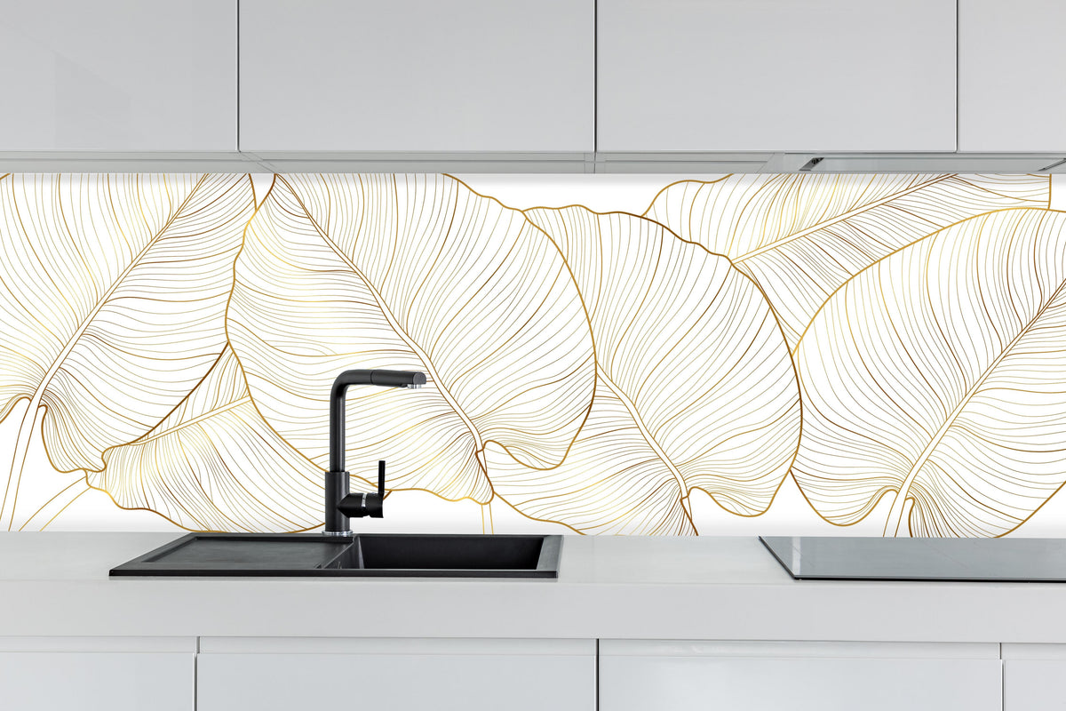 Küche - Elegantes Blatt-Design in Gold und Weiß hinter weißen Hochglanz-Küchenregalen und schwarzem Wasserhahn