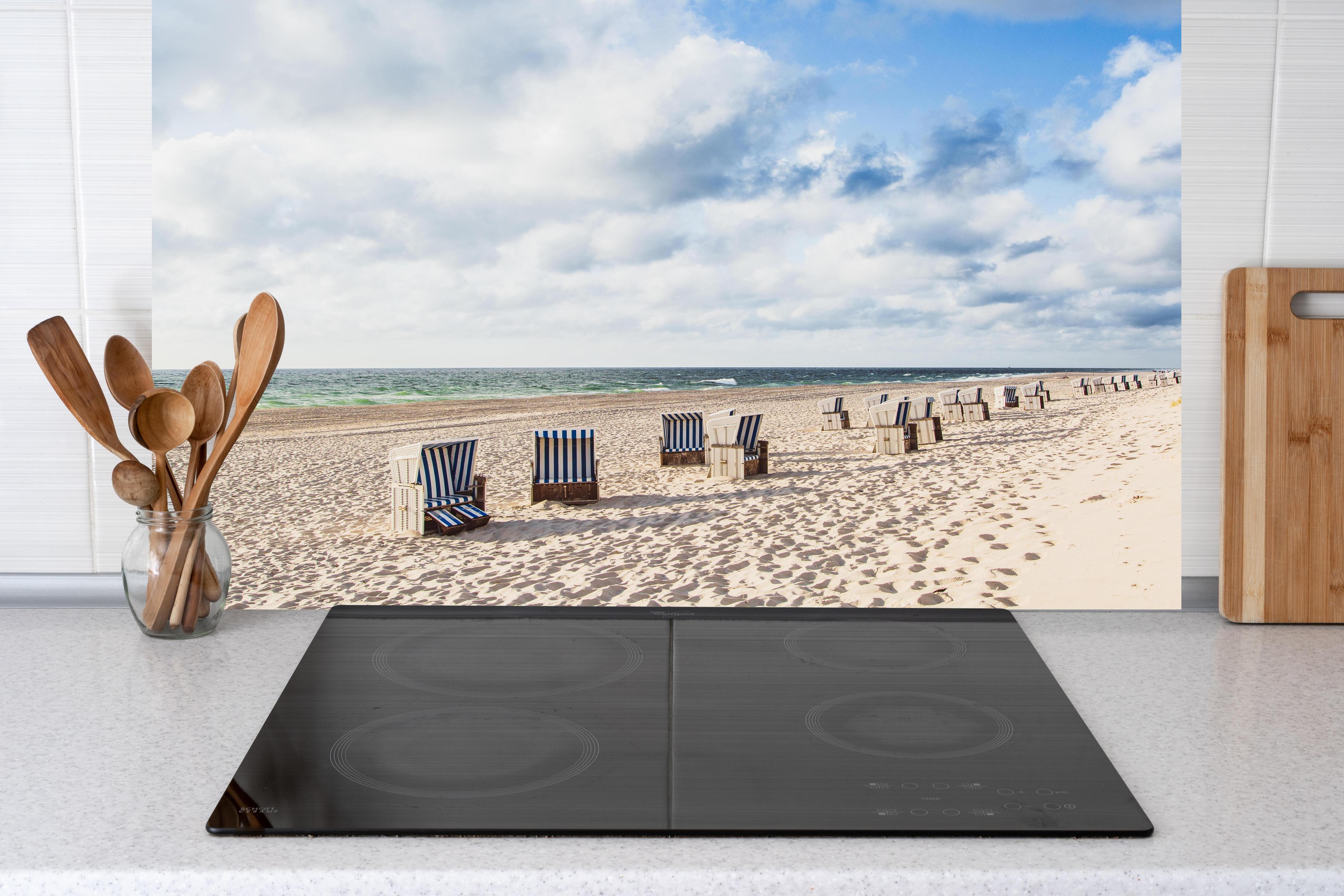 Küche - Entspannte Strandatmosphäre mit blauen und weißen Liegestühlen am Meer hinter weißen Hochglanz-Küchenregalen und schwarzem Wasserhahn