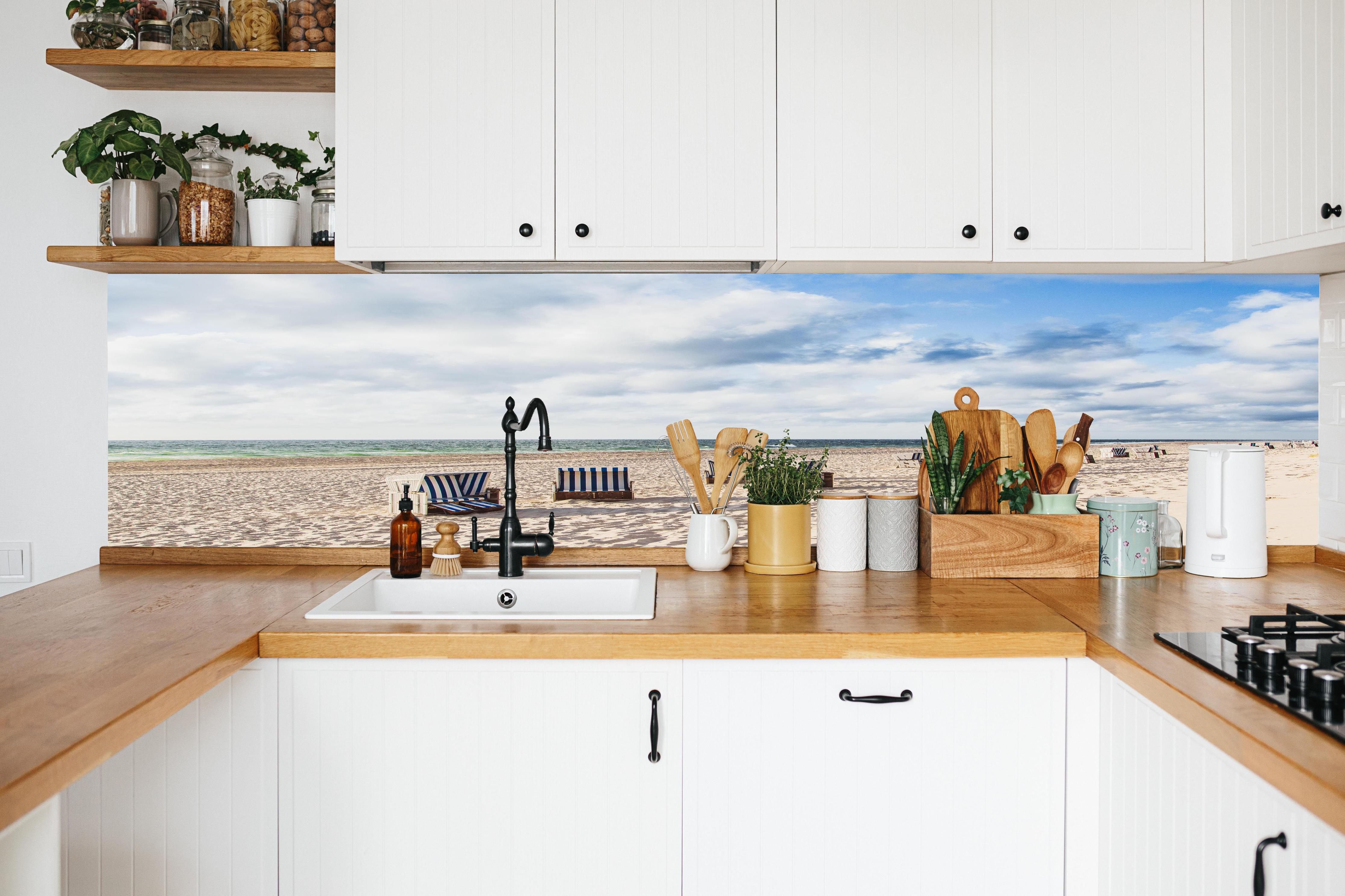 Küche - Entspannte Strandatmosphäre mit blauen und weißen Liegestühlen am Meer hinter weißen Hochglanz-Küchenregalen und schwarzem Wasserhahn