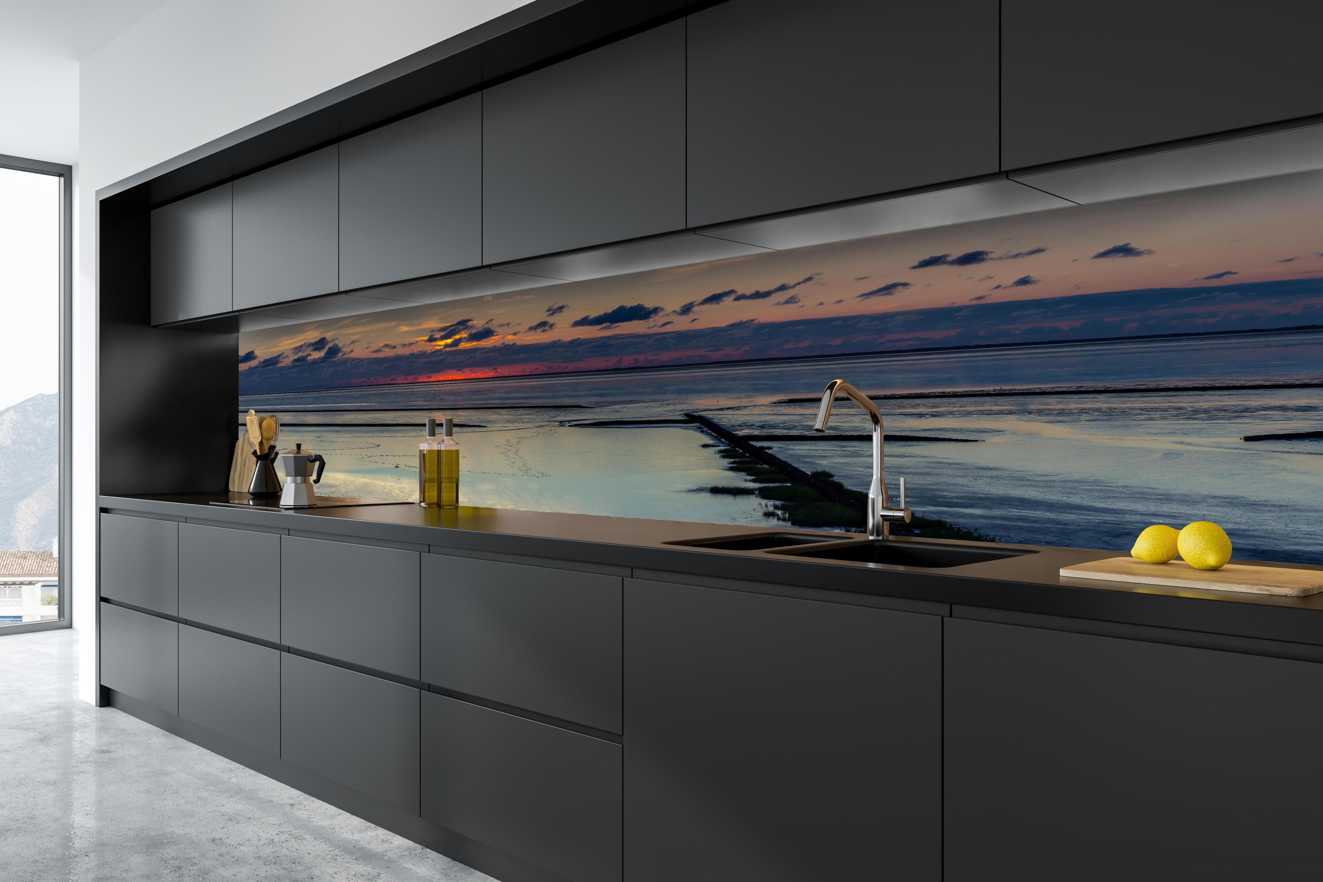 Küche - Faszinierender Sonnenuntergang über einem stillen Gewässer hinter weißen Hochglanz-Küchenregalen und schwarzem Wasserhahn