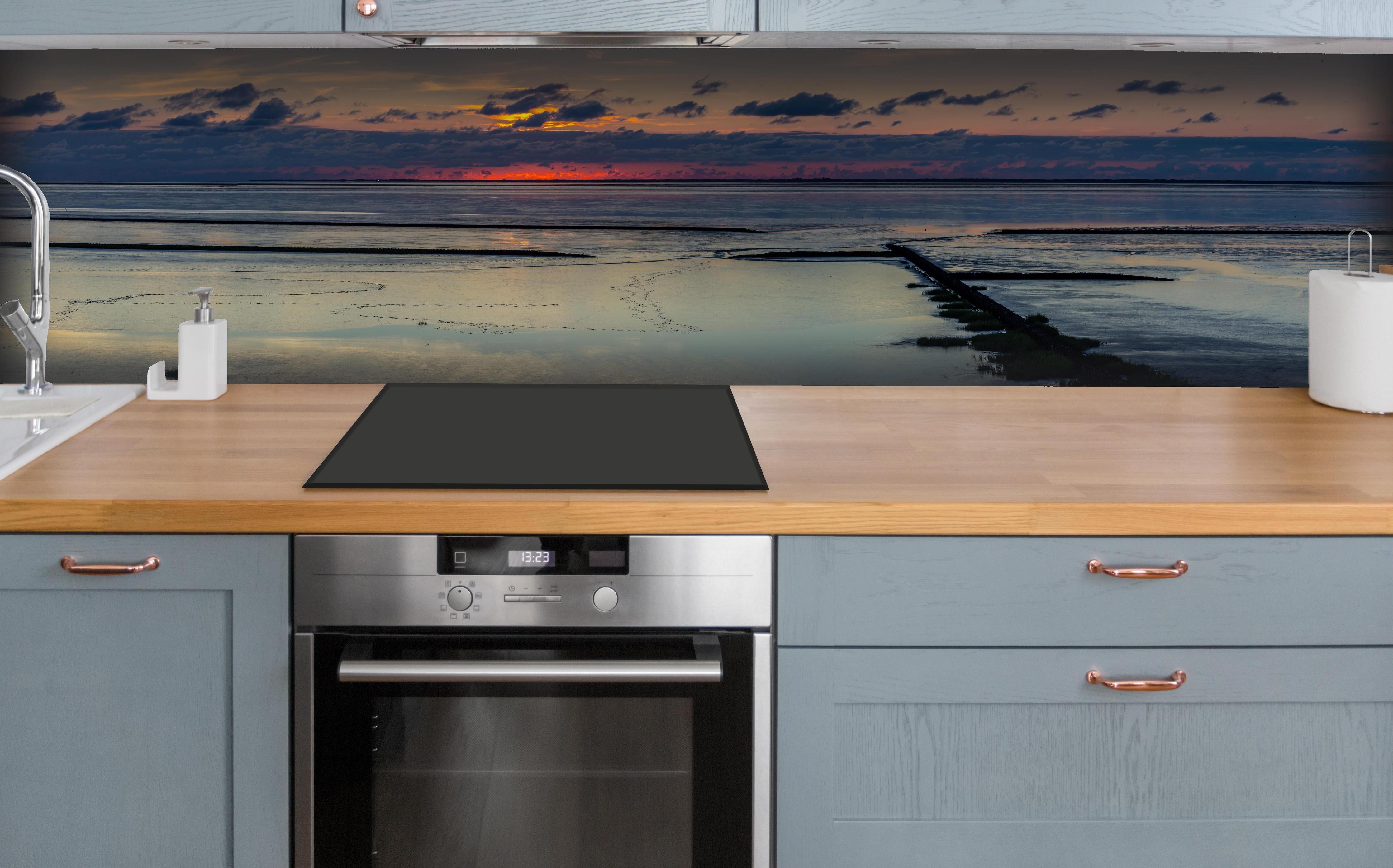 Küche - Faszinierender Sonnenuntergang über einem stillen Gewässer hinter weißen Hochglanz-Küchenregalen und schwarzem Wasserhahn