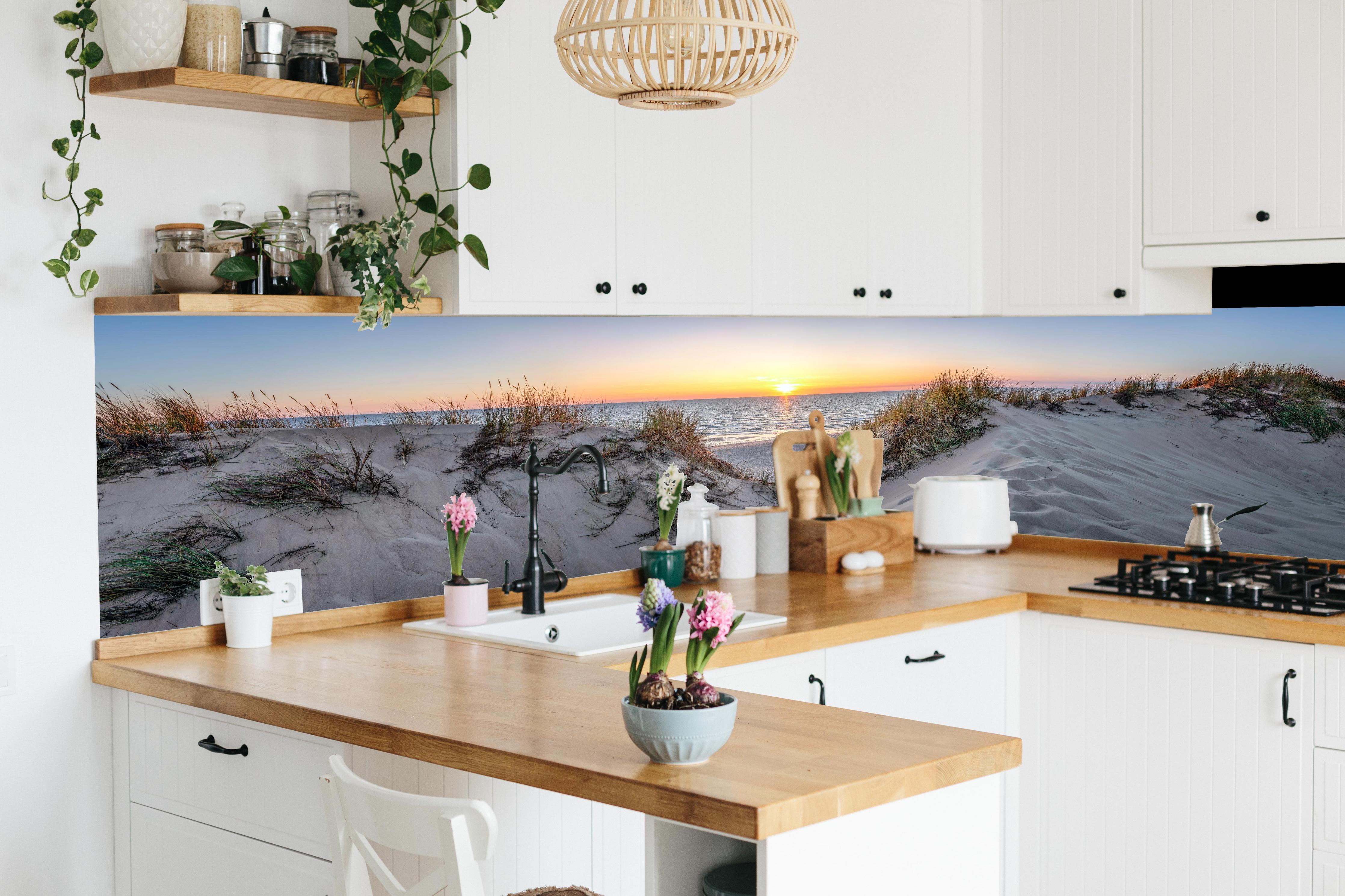 Küche - Faszinierender Sonnenuntergang über einer Sanddüne am Meer hinter weißen Hochglanz-Küchenregalen und schwarzem Wasserhahn