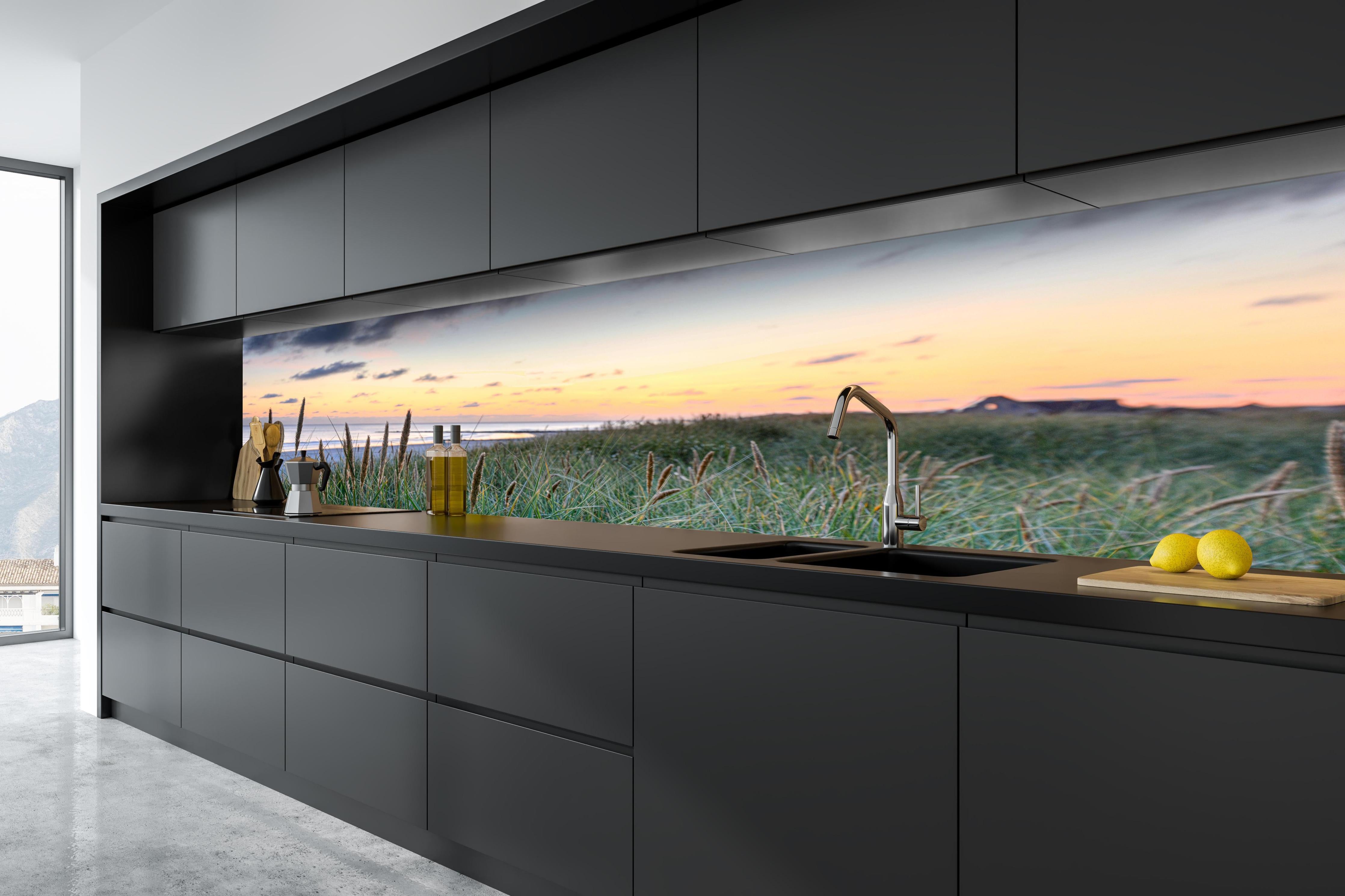 Küche - Friedliche Strandlandschaft mit grünem Gras und sanften Wellen bei Sonnenuntergang hinter weißen Hochglanz-Küchenregalen und schwarzem Wasserhahn