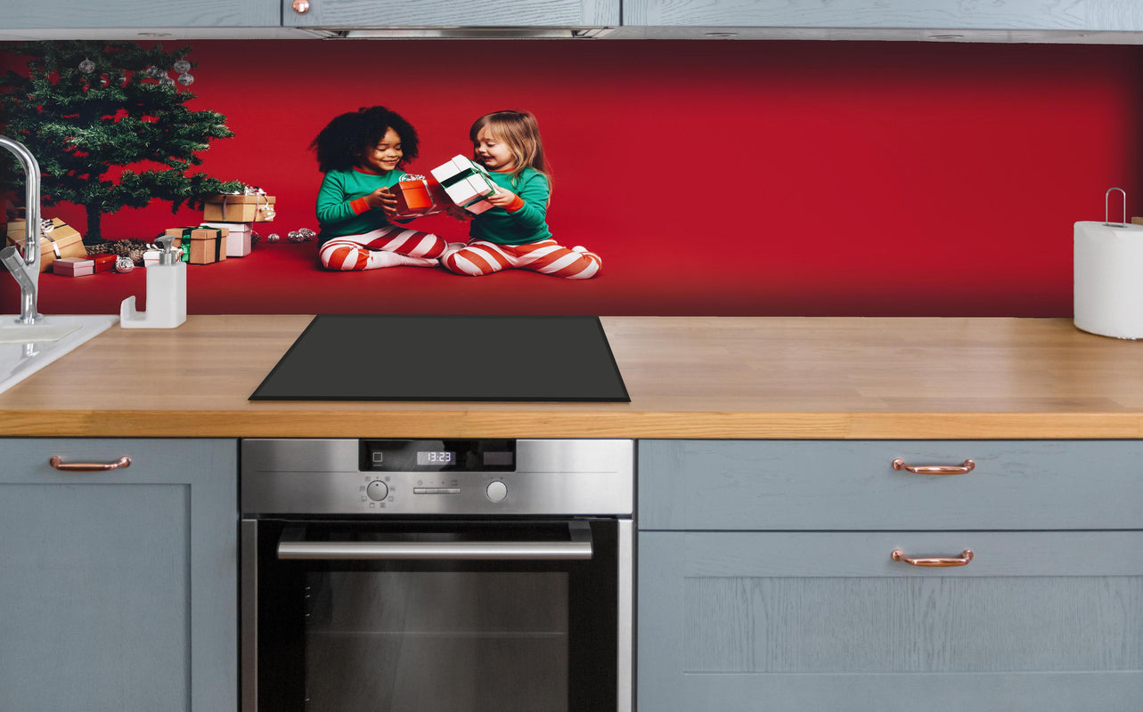 Küche - Fröhliche Kinder tauschen Weihnachtsgeschenke aus hinter weißen Hochglanz-Küchenregalen und schwarzem Wasserhahn