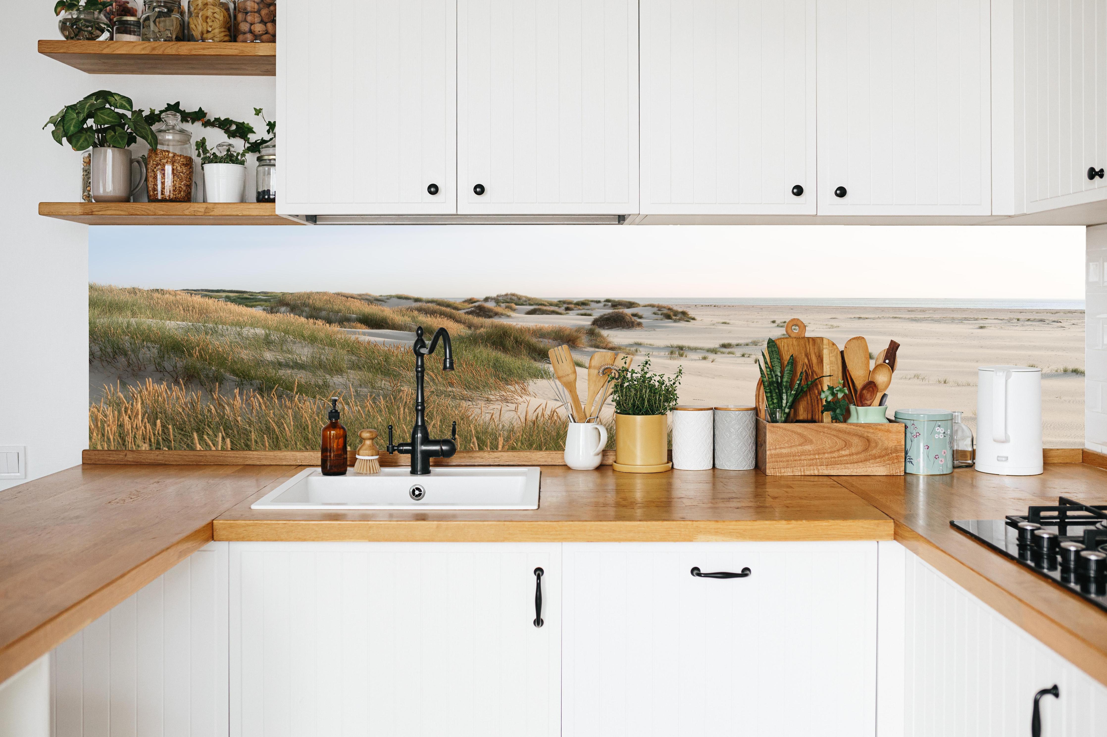 Küche - Harmonische Strandlandschaft mit sanften Sanddünen und Strandgräsern hinter weißen Hochglanz-Küchenregalen und schwarzem Wasserhahn