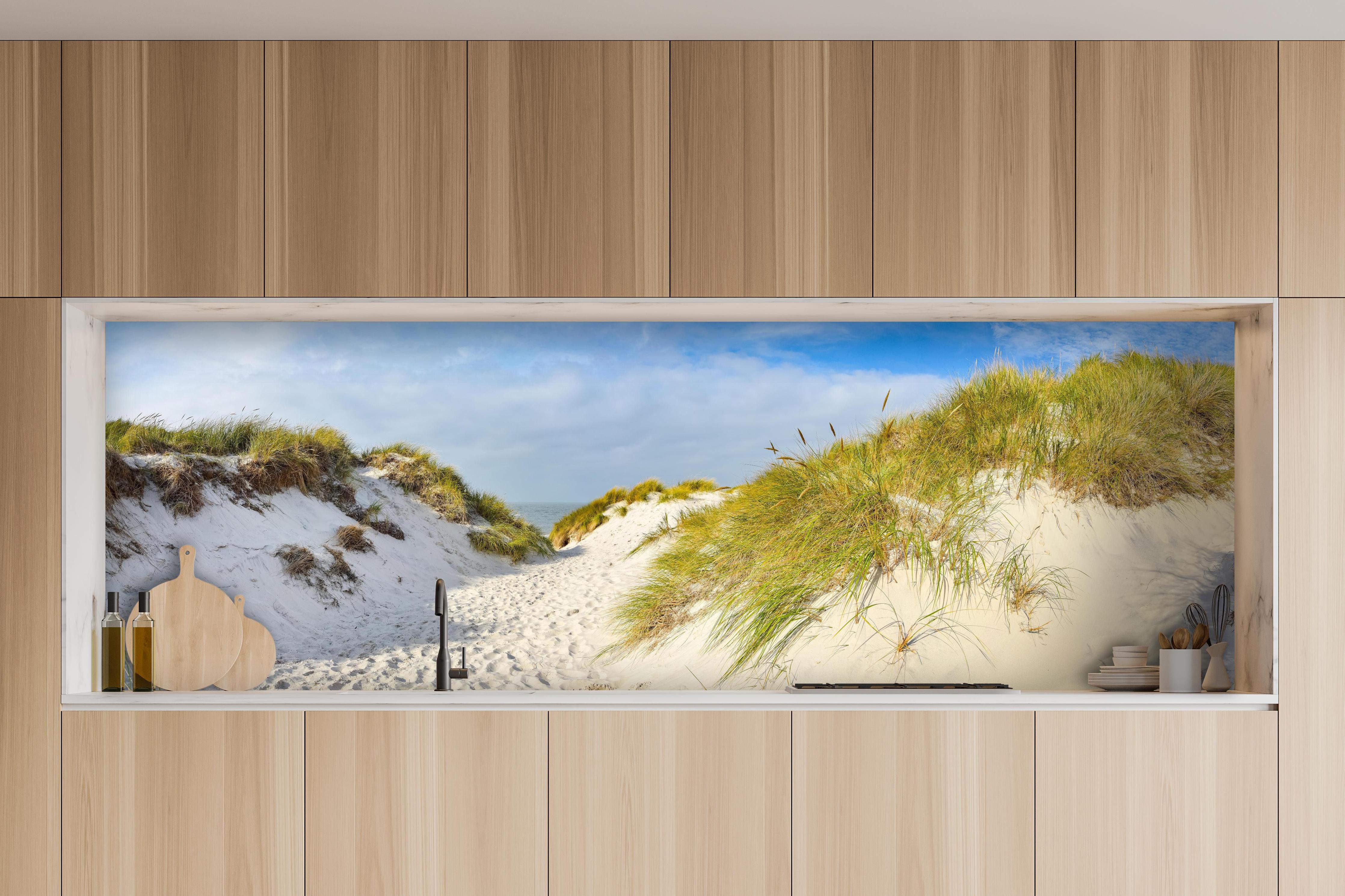 Küche - Idyllische Dünenlandschaft mit feinem Sand und grünem Gras hinter weißen Hochglanz-Küchenregalen und schwarzem Wasserhahn