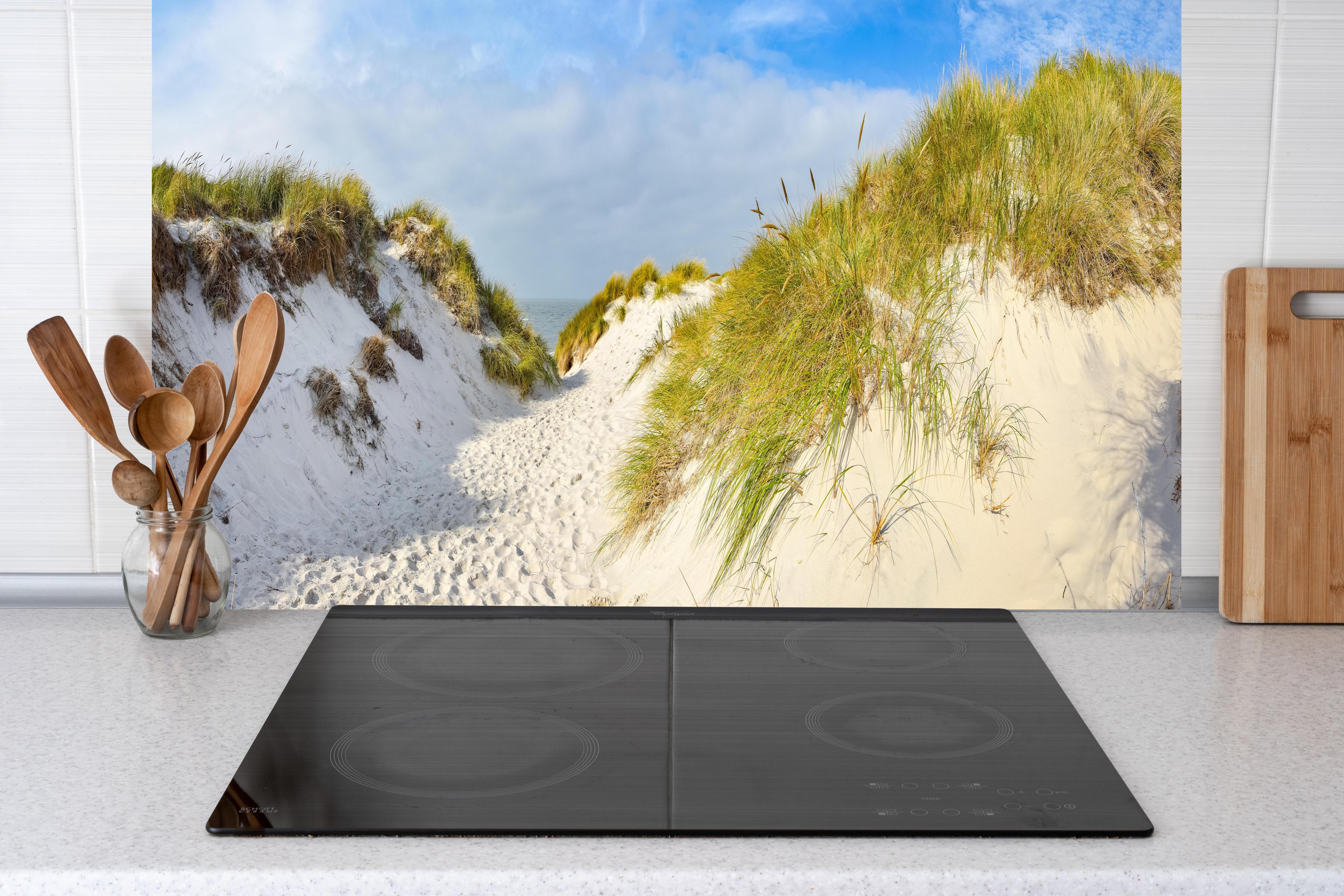 Küche - Idyllische Dünenlandschaft mit feinem Sand und grünem Gras hinter weißen Hochglanz-Küchenregalen und schwarzem Wasserhahn