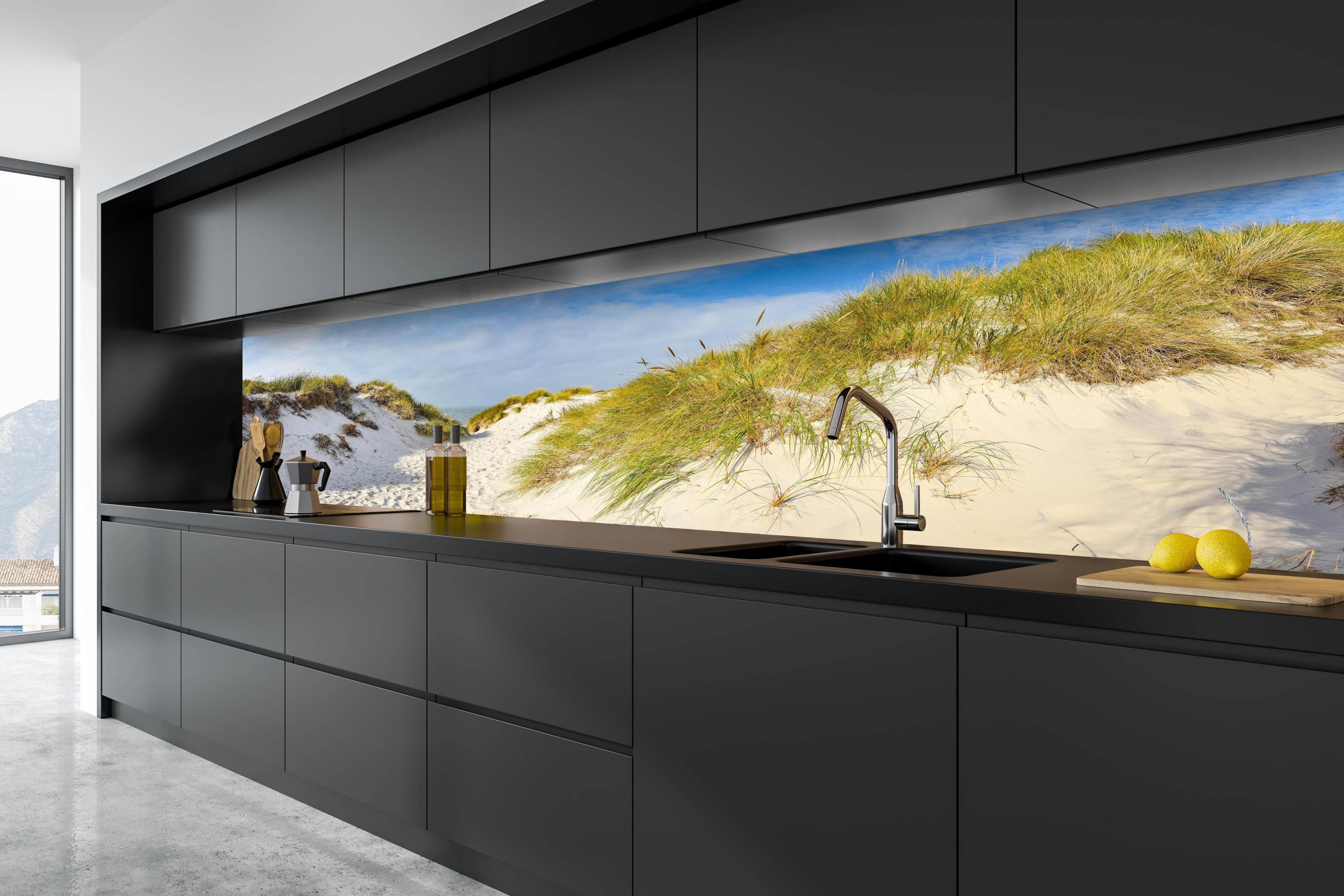 Küche - Idyllische Dünenlandschaft mit feinem Sand und grünem Gras hinter weißen Hochglanz-Küchenregalen und schwarzem Wasserhahn