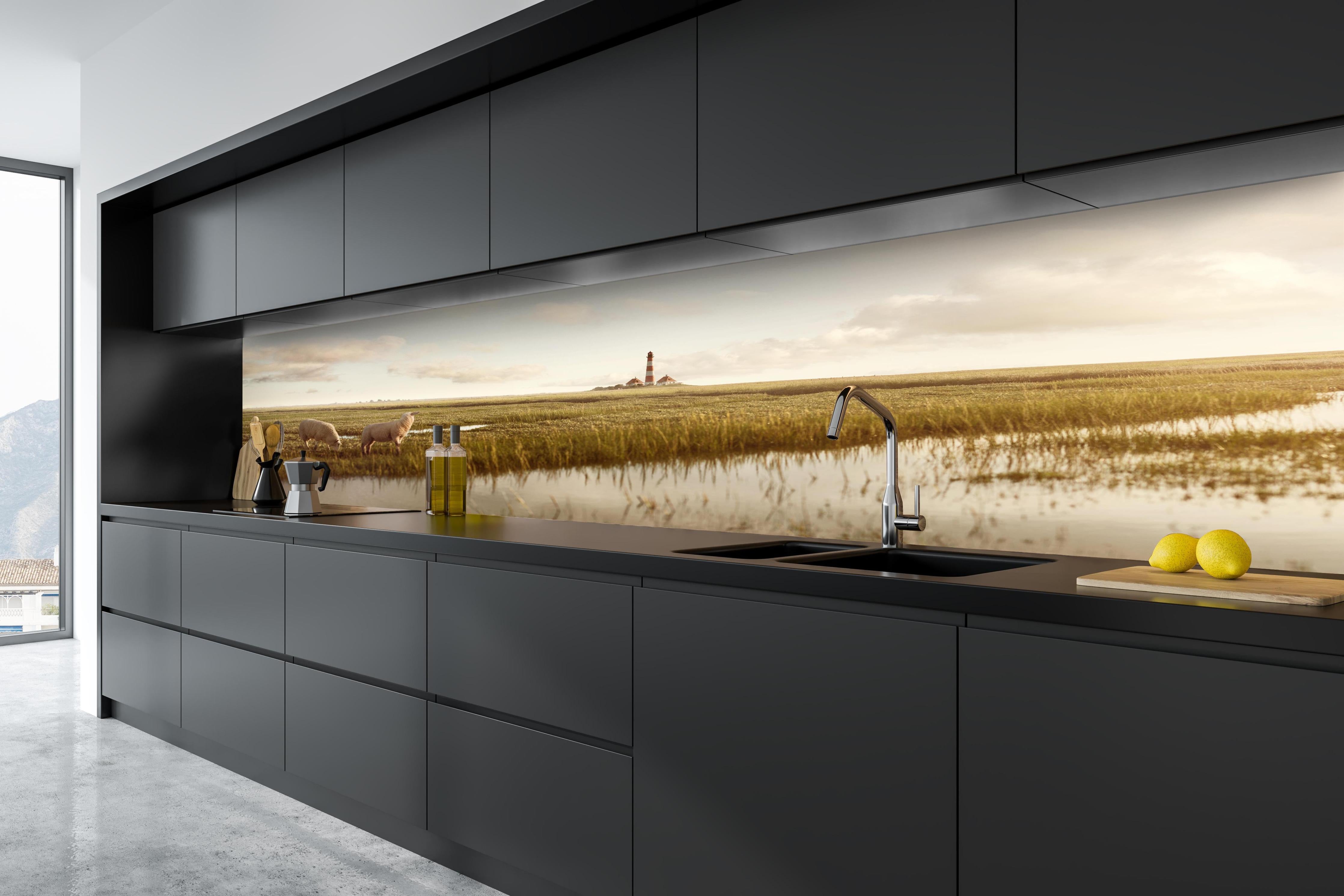 Küche - Idyllische Kulisse mit Schafen und einem Leuchtturm in ruhiger Küstenlandschaft hinter weißen Hochglanz-Küchenregalen und schwarzem Wasserhahn