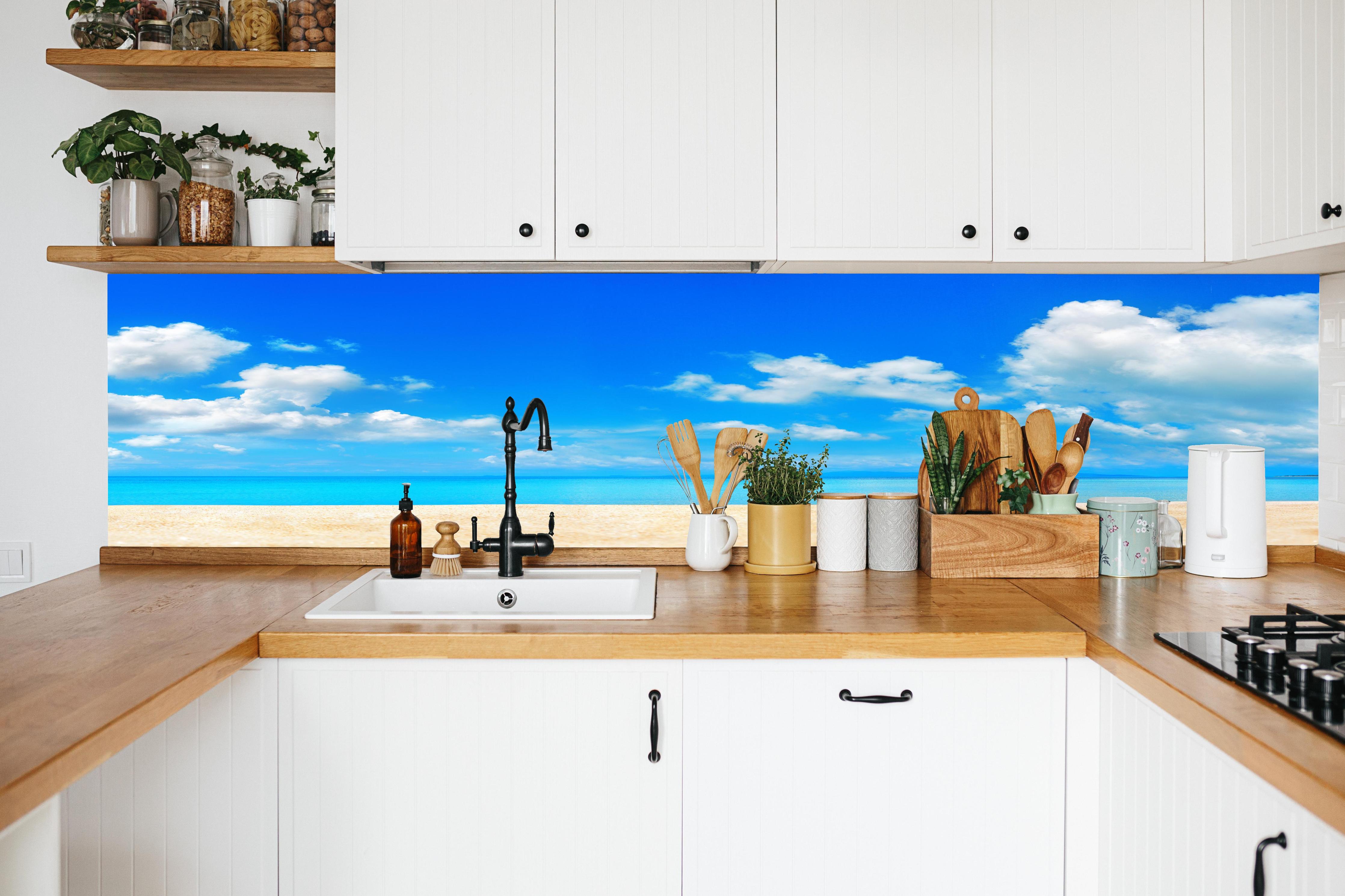 Küche - Idyllische Strandlandschaft mit klarem Wasser und blauem Himmel hinter weißen Hochglanz-Küchenregalen und schwarzem Wasserhahn