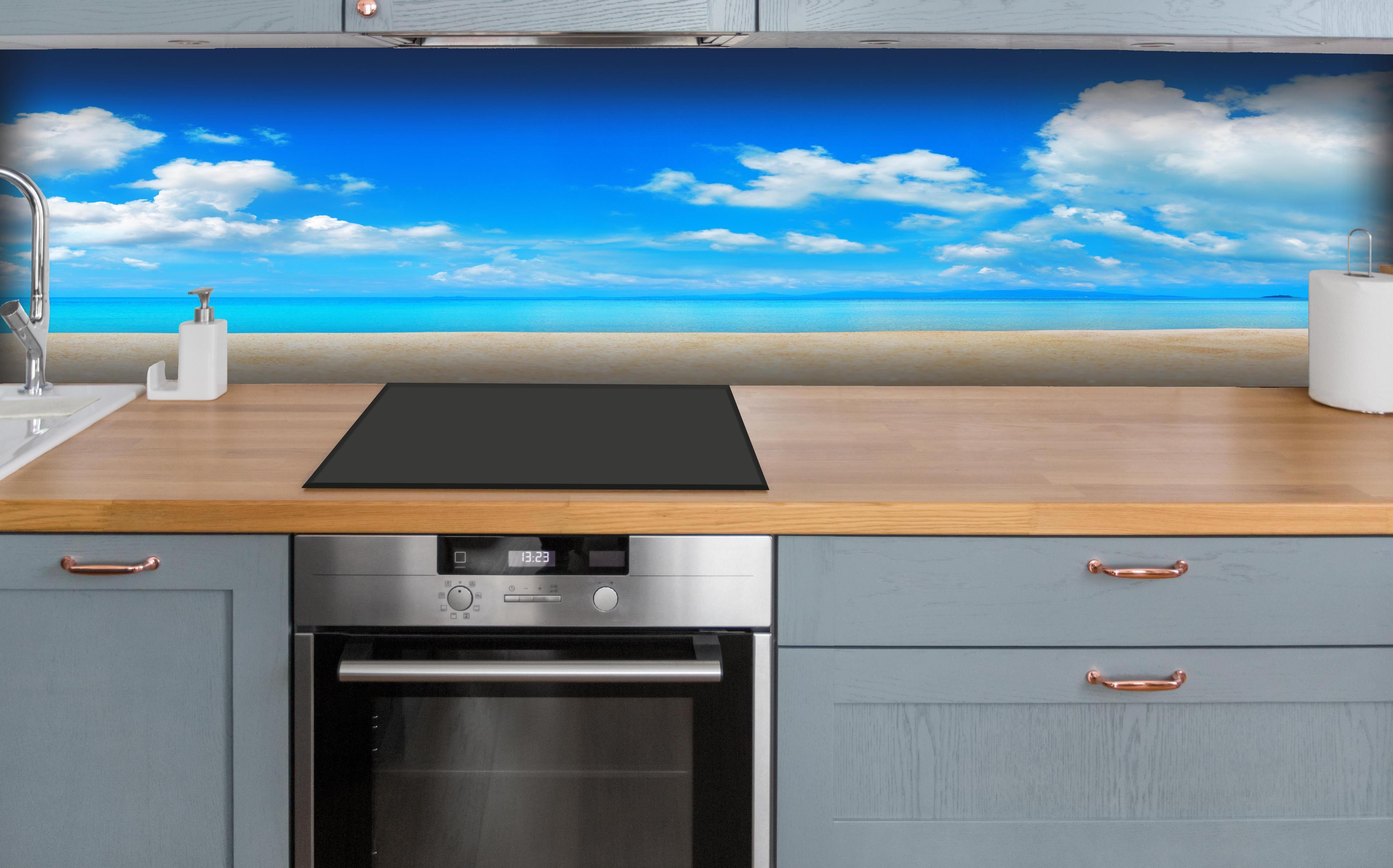 Küche - Idyllische Strandlandschaft mit klarem Wasser und blauem Himmel hinter weißen Hochglanz-Küchenregalen und schwarzem Wasserhahn