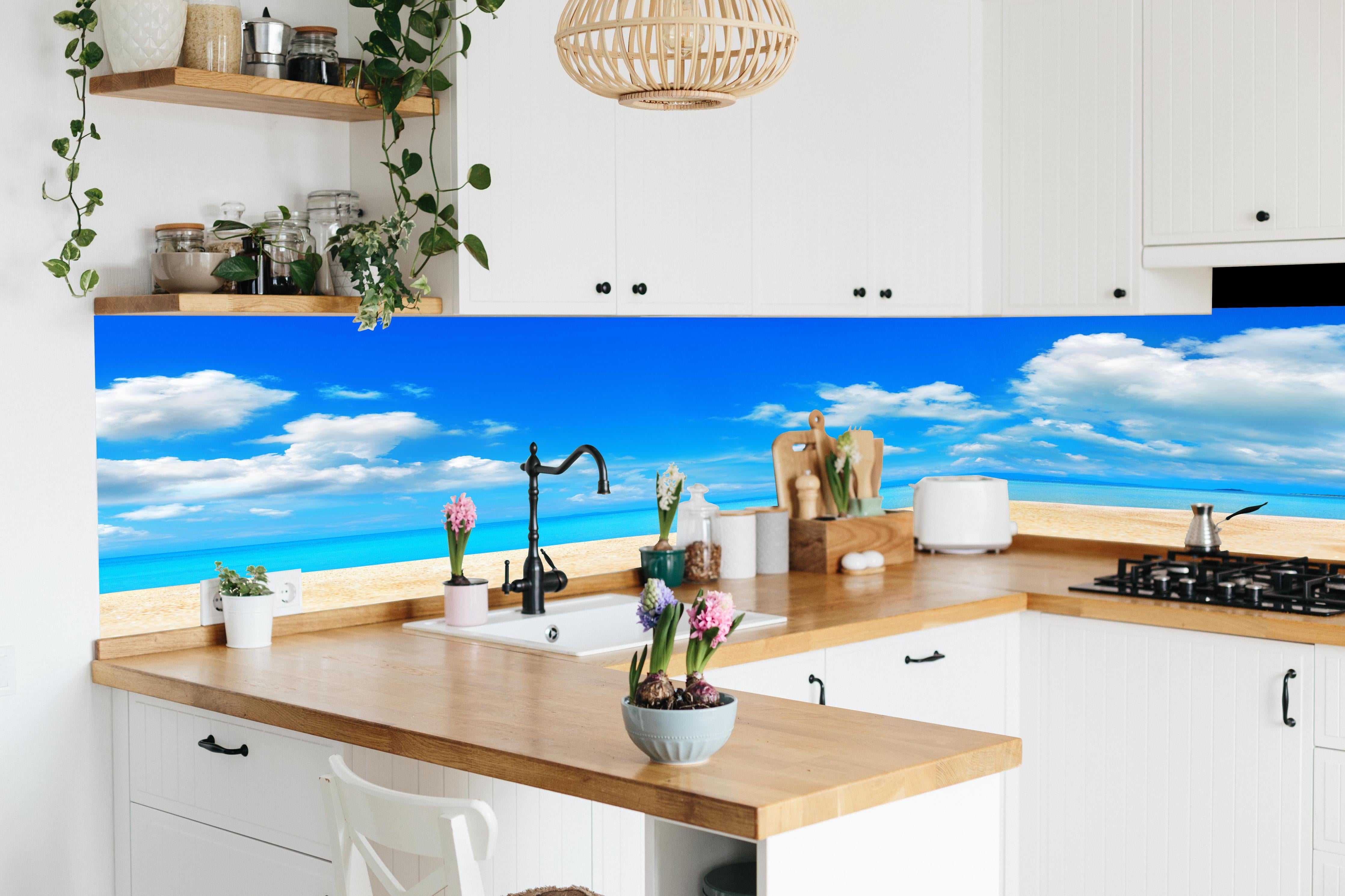 Küche - Idyllische Strandlandschaft mit klarem Wasser und blauem Himmel hinter weißen Hochglanz-Küchenregalen und schwarzem Wasserhahn