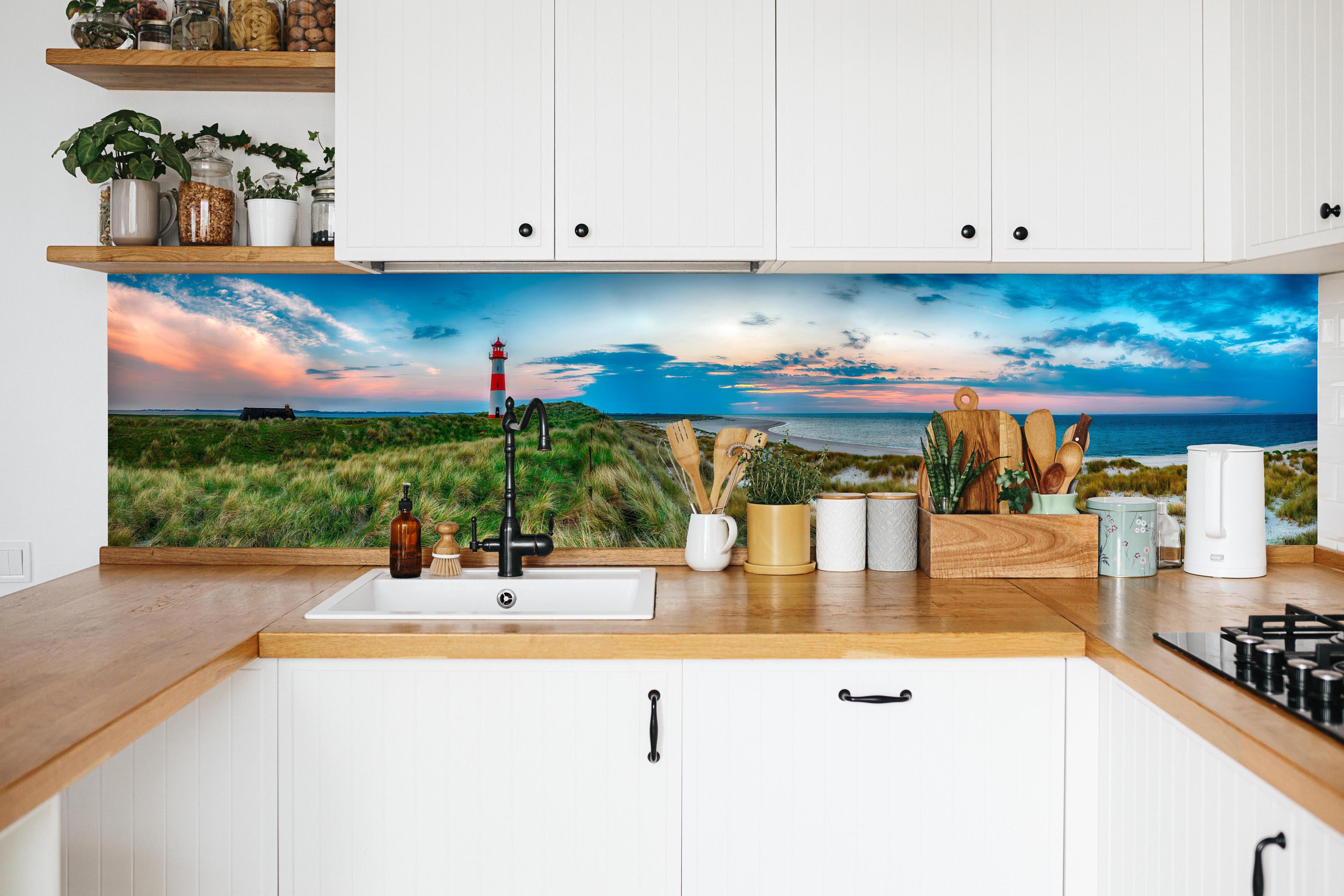 Küche - Idyllischer Leuchtturm mit traumhaften Ausblick auf den Sonnenuntergang am Meer hinter weißen Hochglanz-Küchenregalen und schwarzem Wasserhahn