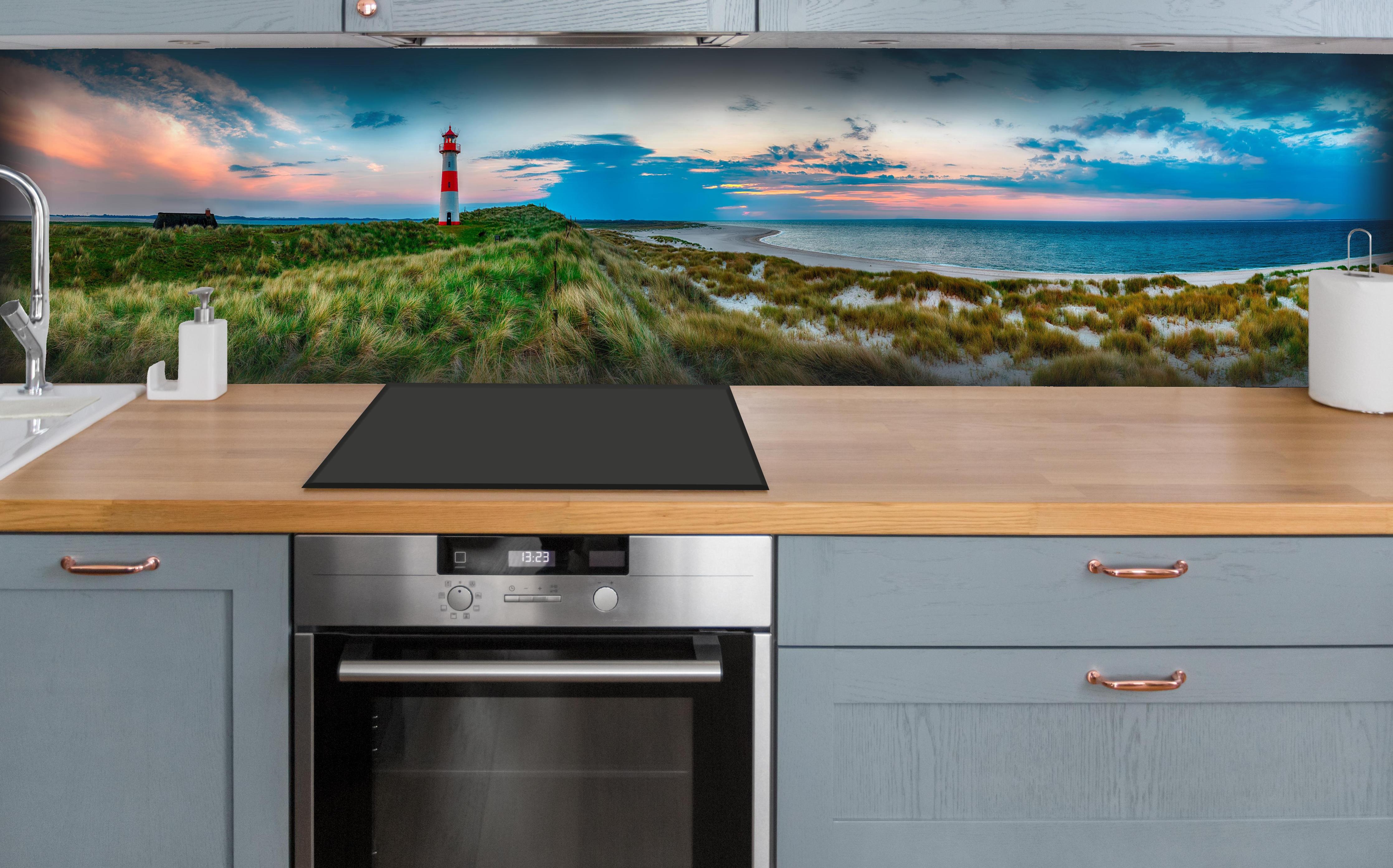 Küche - Idyllischer Leuchtturm mit traumhaften Ausblick auf den Sonnenuntergang am Meer hinter weißen Hochglanz-Küchenregalen und schwarzem Wasserhahn