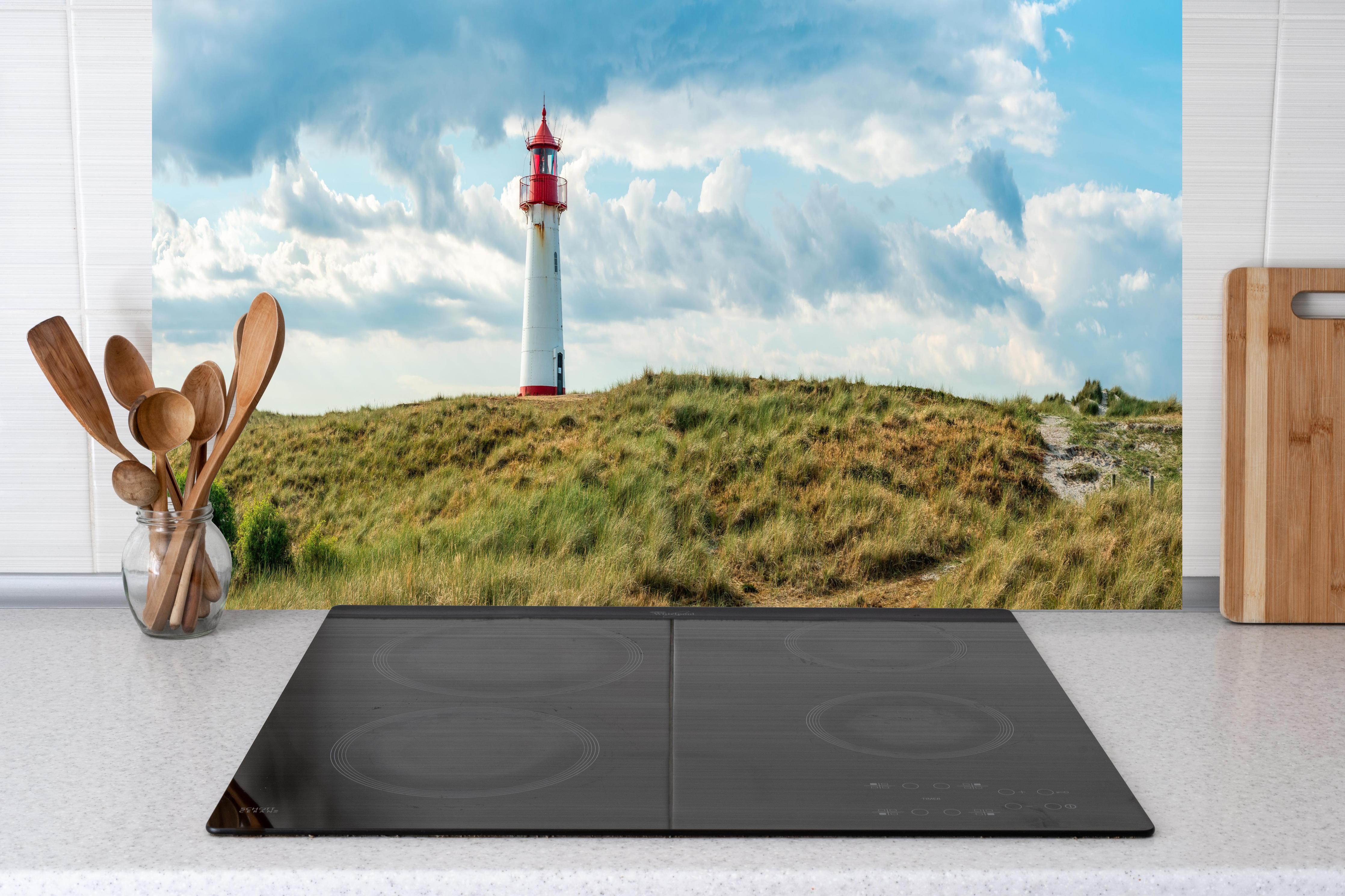 Küche - Idyllischer Leuchtturm umgeben von weiten Grasfeldern hinter weißen Hochglanz-Küchenregalen und schwarzem Wasserhahn