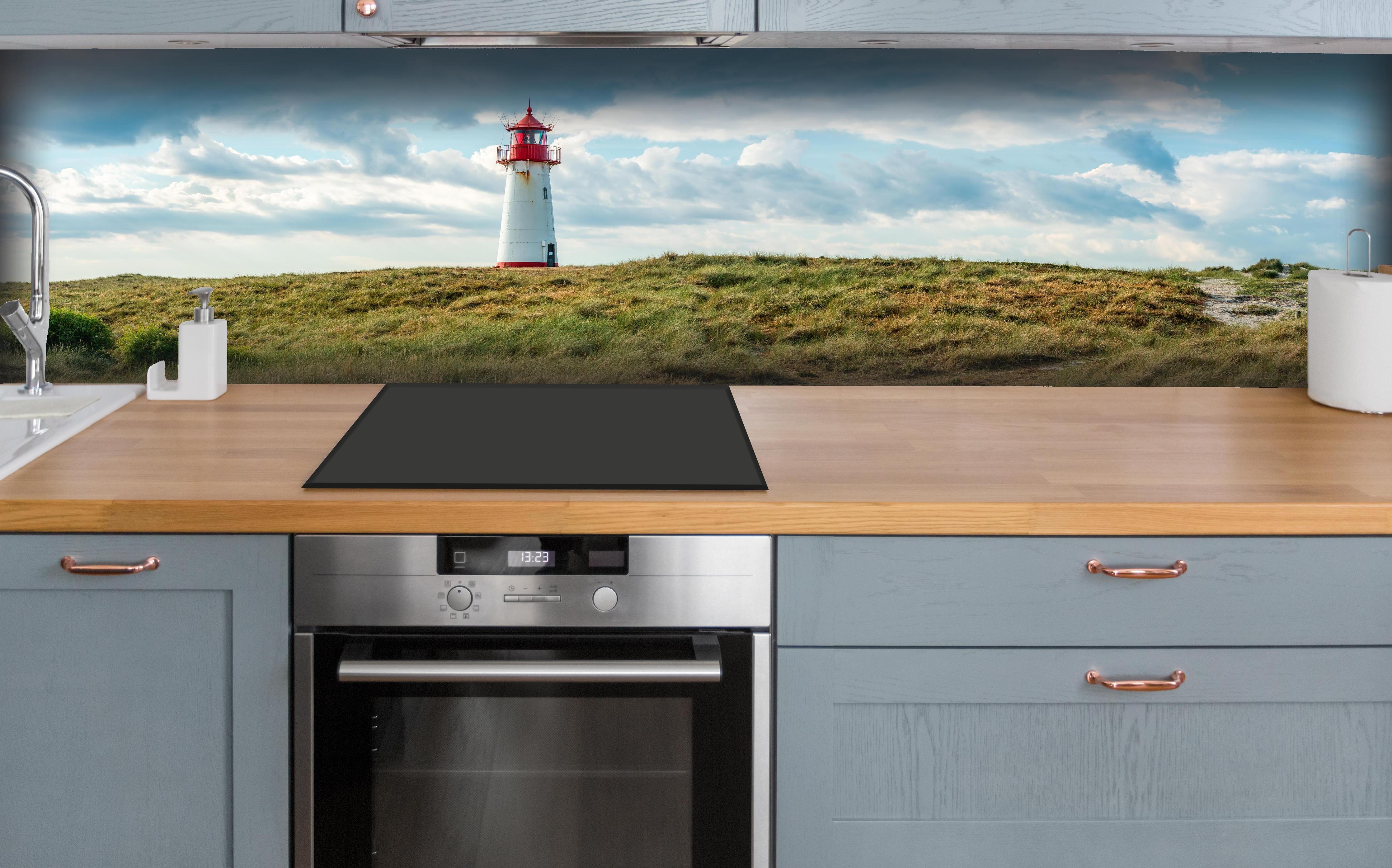 Küche - Idyllischer Leuchtturm umgeben von weiten Grasfeldern hinter weißen Hochglanz-Küchenregalen und schwarzem Wasserhahn