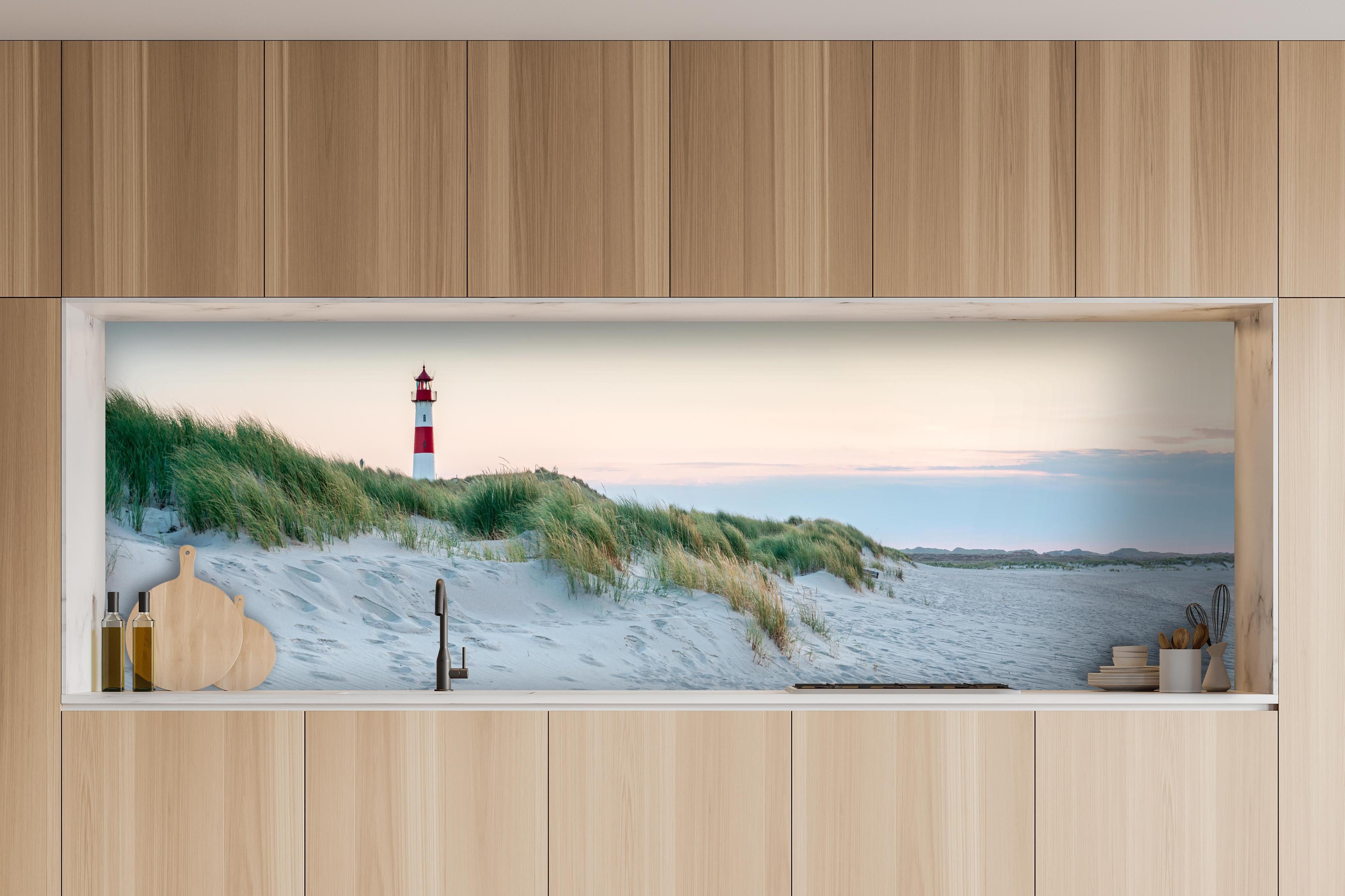 Küche - Idyllischer Leuchtturm zwischen Sanddünen und sanften Wellen hinter weißen Hochglanz-Küchenregalen und schwarzem Wasserhahn