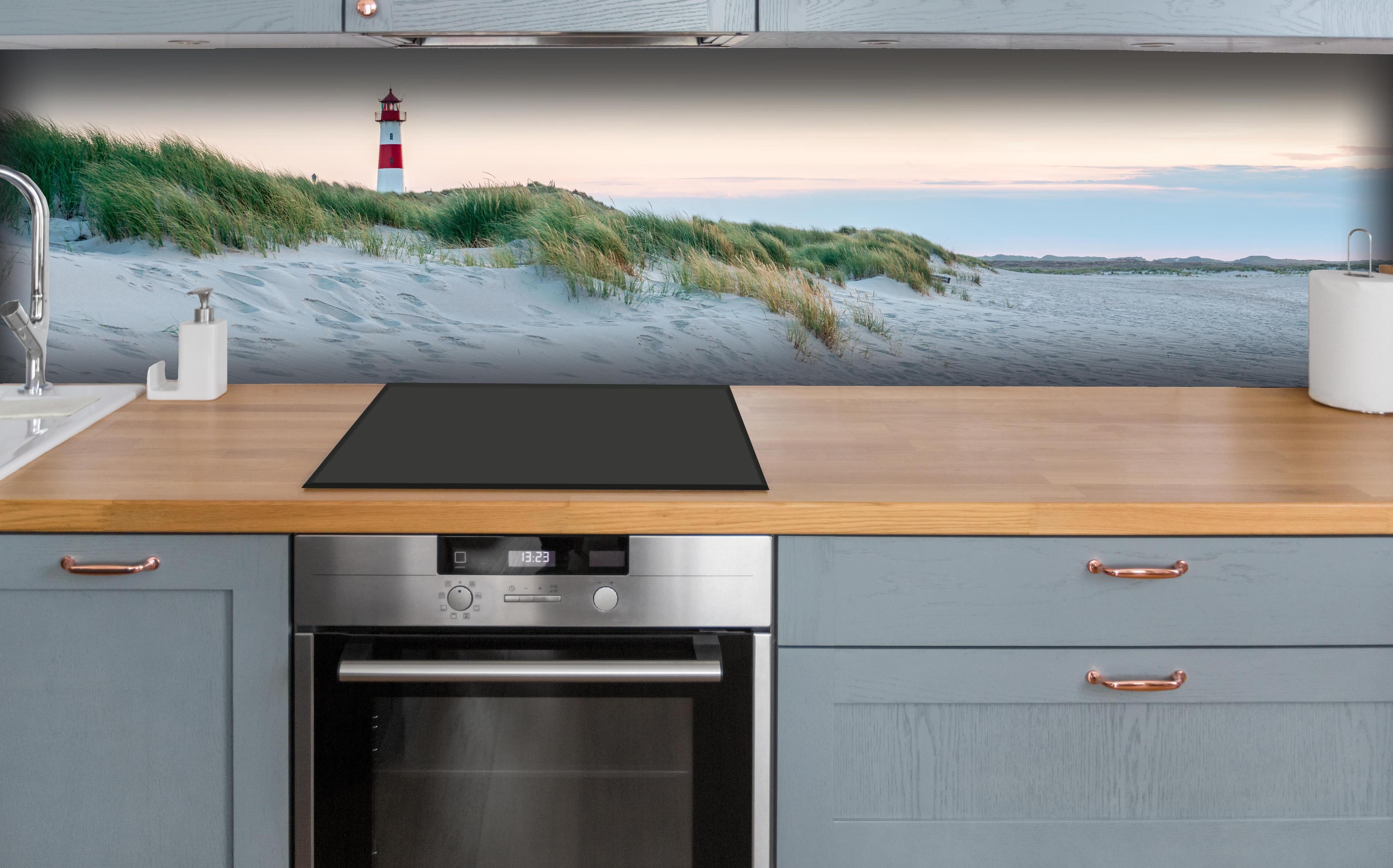 Küche - Idyllischer Leuchtturm zwischen Sanddünen und sanften Wellen hinter weißen Hochglanz-Küchenregalen und schwarzem Wasserhahn
