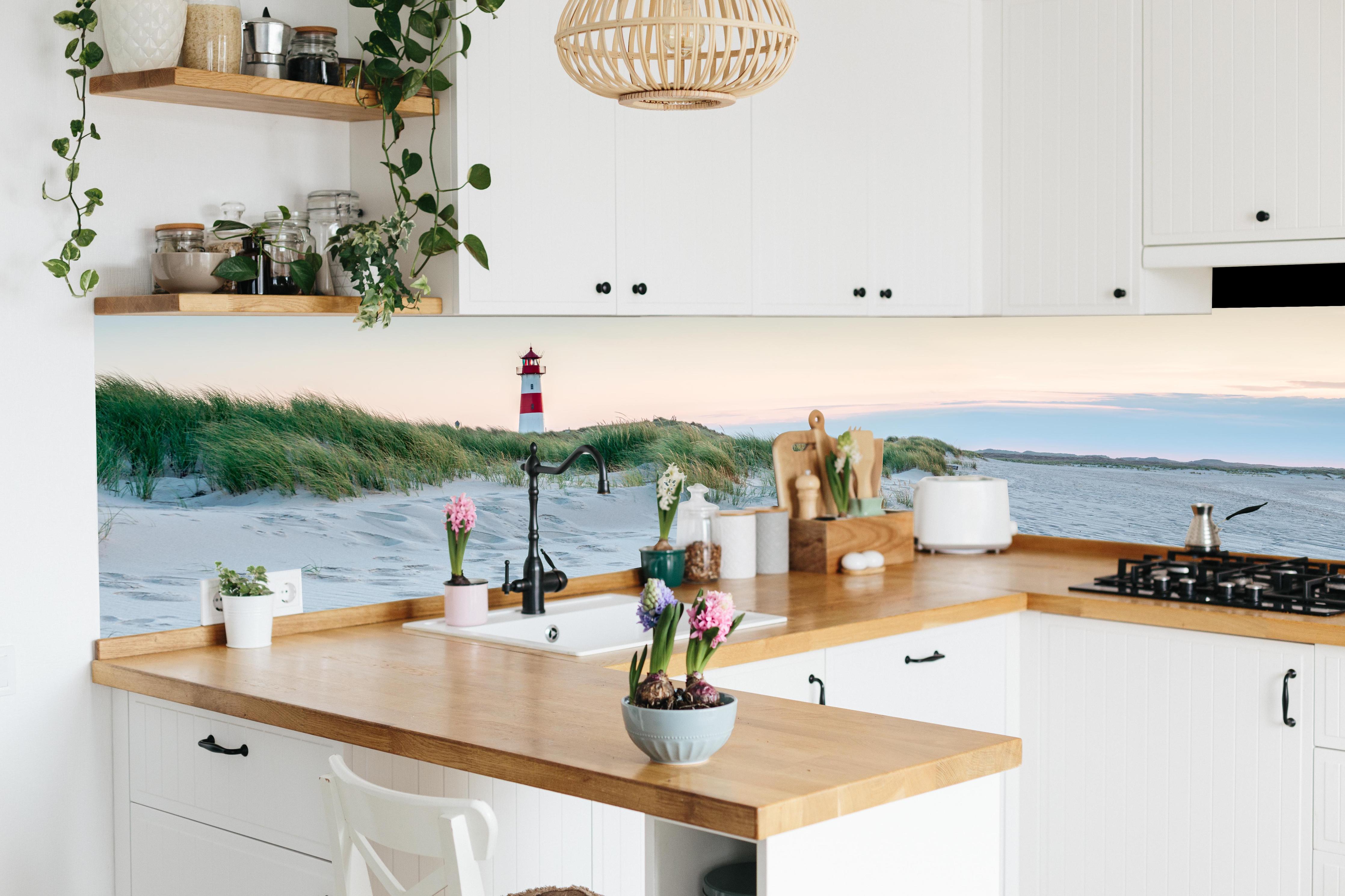 Küche - Idyllischer Leuchtturm zwischen Sanddünen und sanften Wellen hinter weißen Hochglanz-Küchenregalen und schwarzem Wasserhahn
