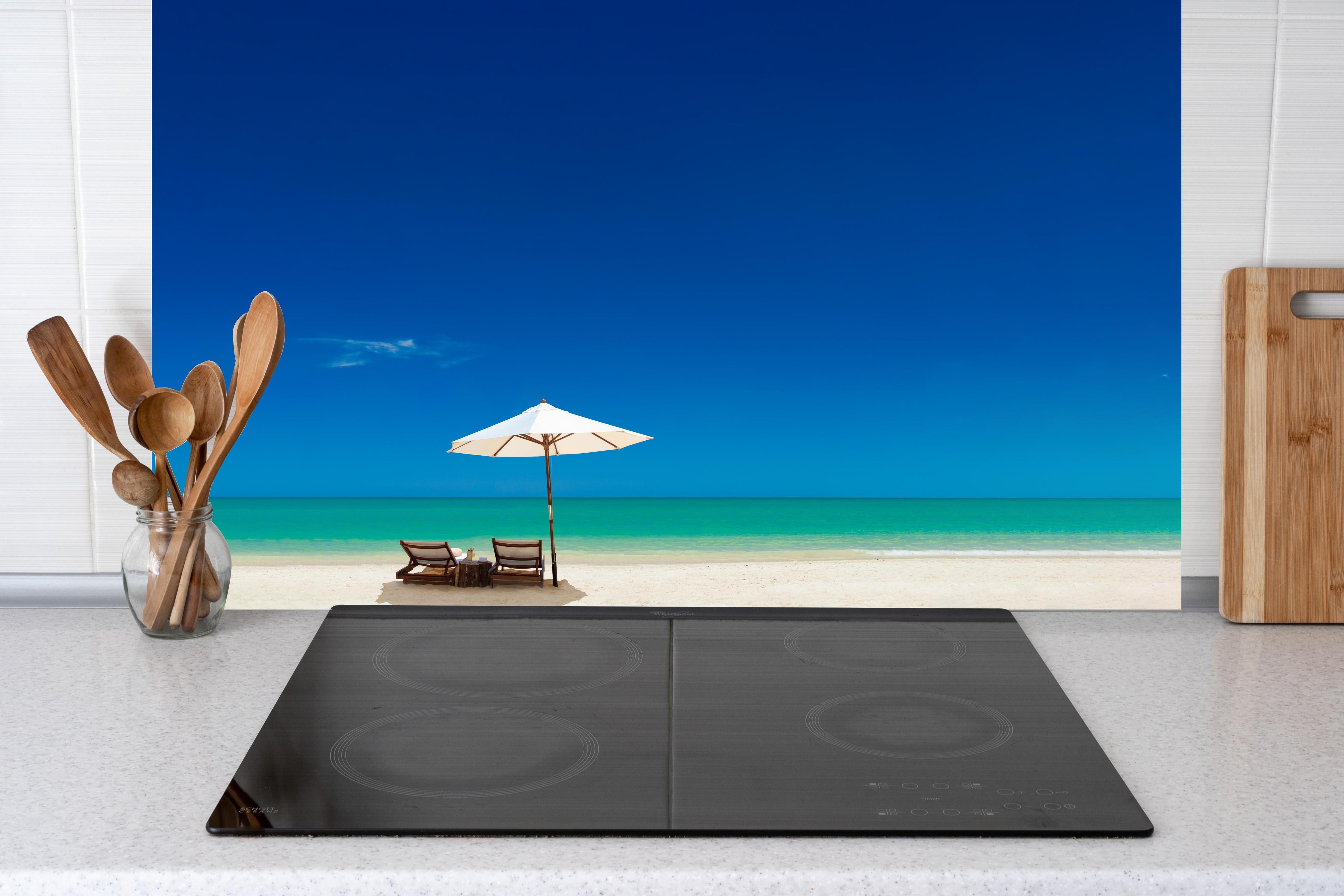 Küche - Idyllischer Strand mit Liegen und Sonnenschirm unter blauem Himmel hinter weißen Hochglanz-Küchenregalen und schwarzem Wasserhahn