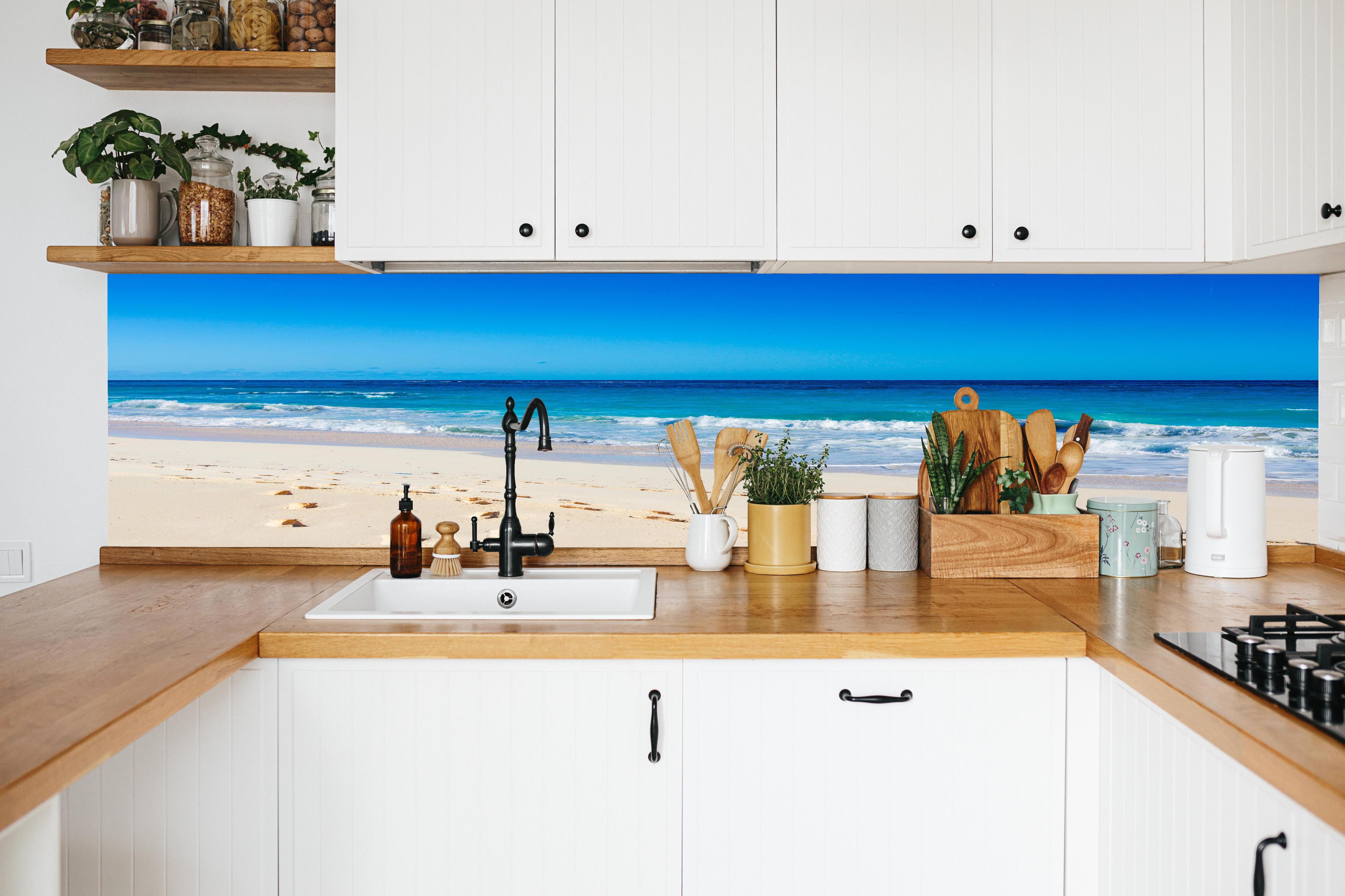 Küche - Idyllischer Strand mit feinem Sand und türkisfarbenem Wasser hinter weißen Hochglanz-Küchenregalen und schwarzem Wasserhahn