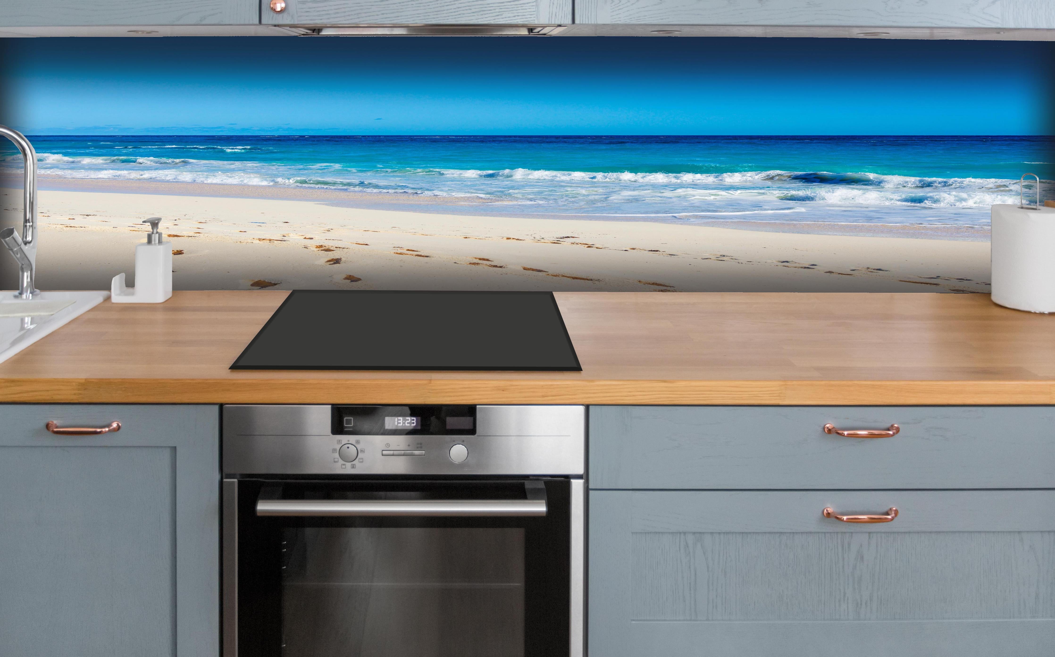 Küche - Idyllischer Strand mit feinem Sand und türkisfarbenem Wasser hinter weißen Hochglanz-Küchenregalen und schwarzem Wasserhahn