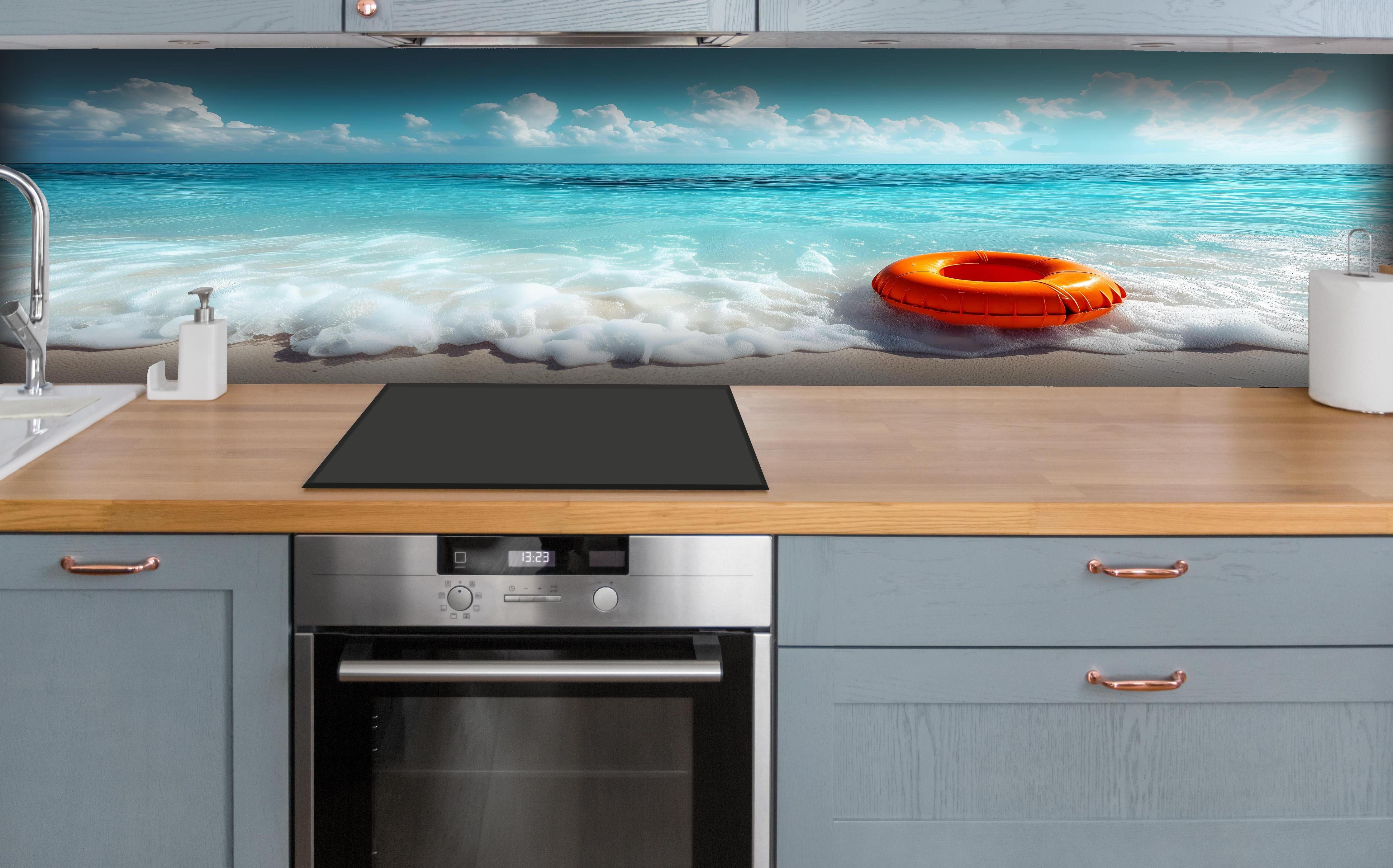 Küche - Idyllischer Strand mit orangefarbener Schwimmringen und klarblauem Wasser hinter weißen Hochglanz-Küchenregalen und schwarzem Wasserhahn