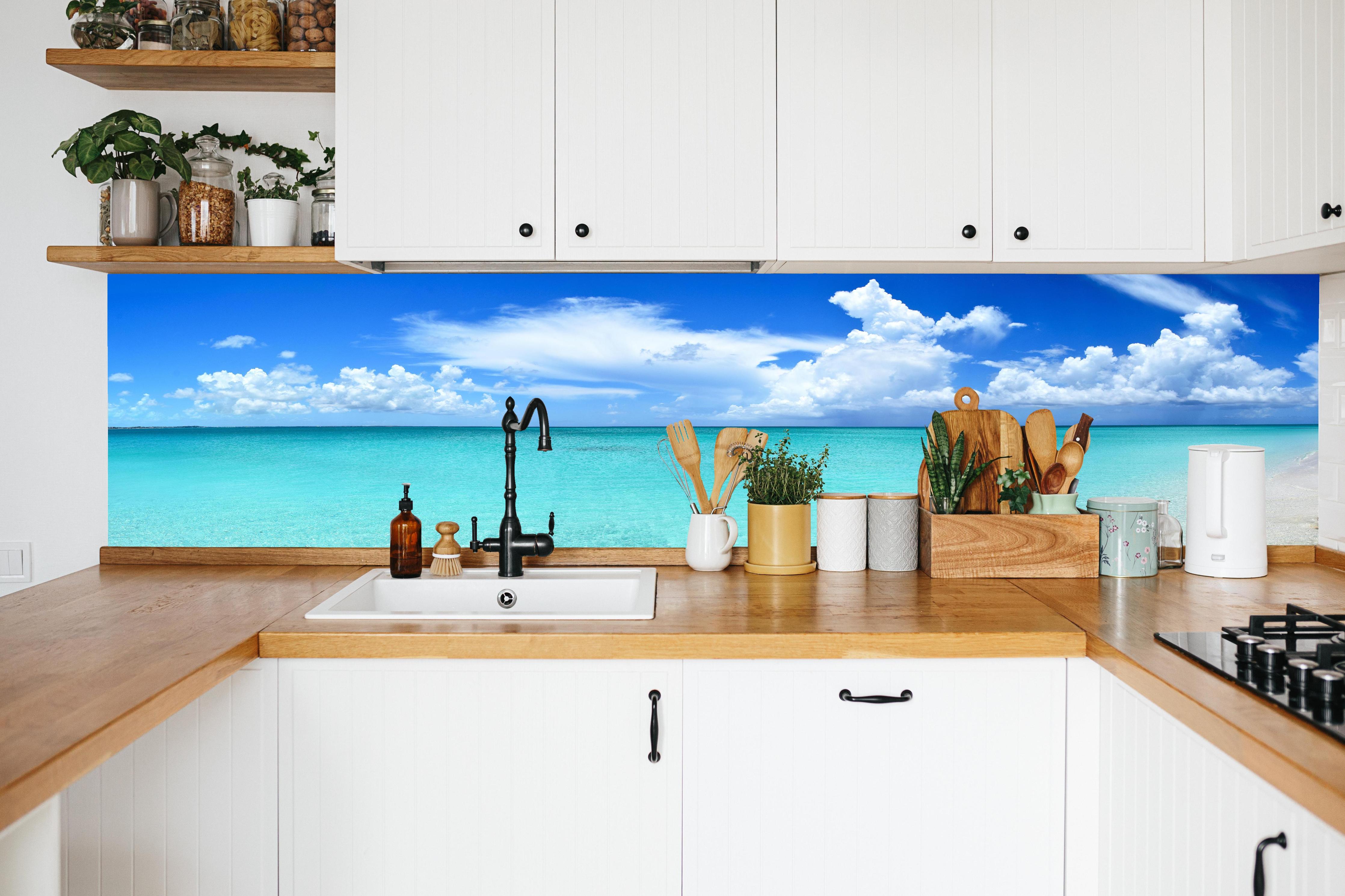 Küche - Idyllischer Strand unter einem strahlend blauen Himmel hinter weißen Hochglanz-Küchenregalen und schwarzem Wasserhahn