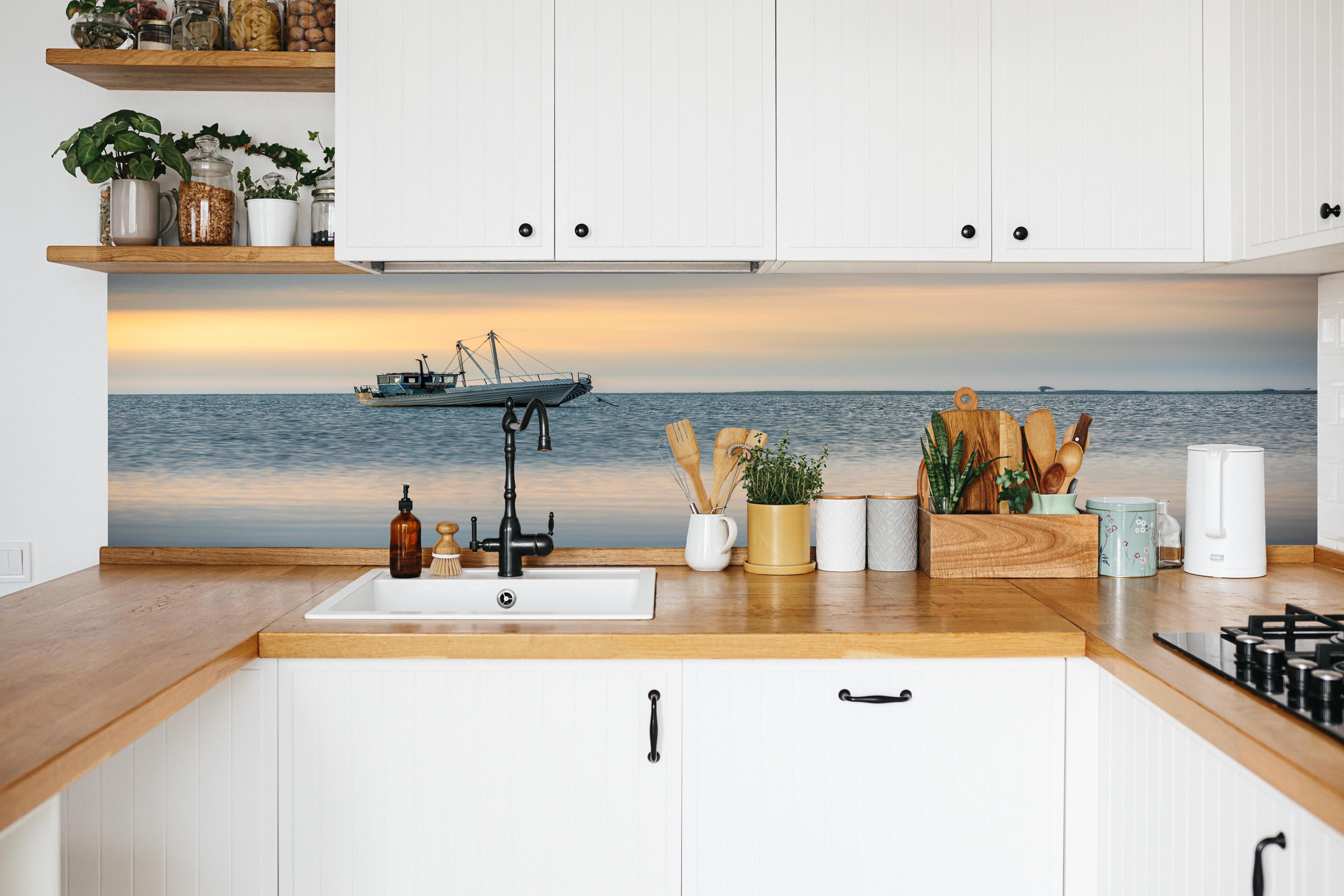 Küche - Idyllisches Boot auf ruhigem Wasser bei Sonnenuntergang hinter weißen Hochglanz-Küchenregalen und schwarzem Wasserhahn