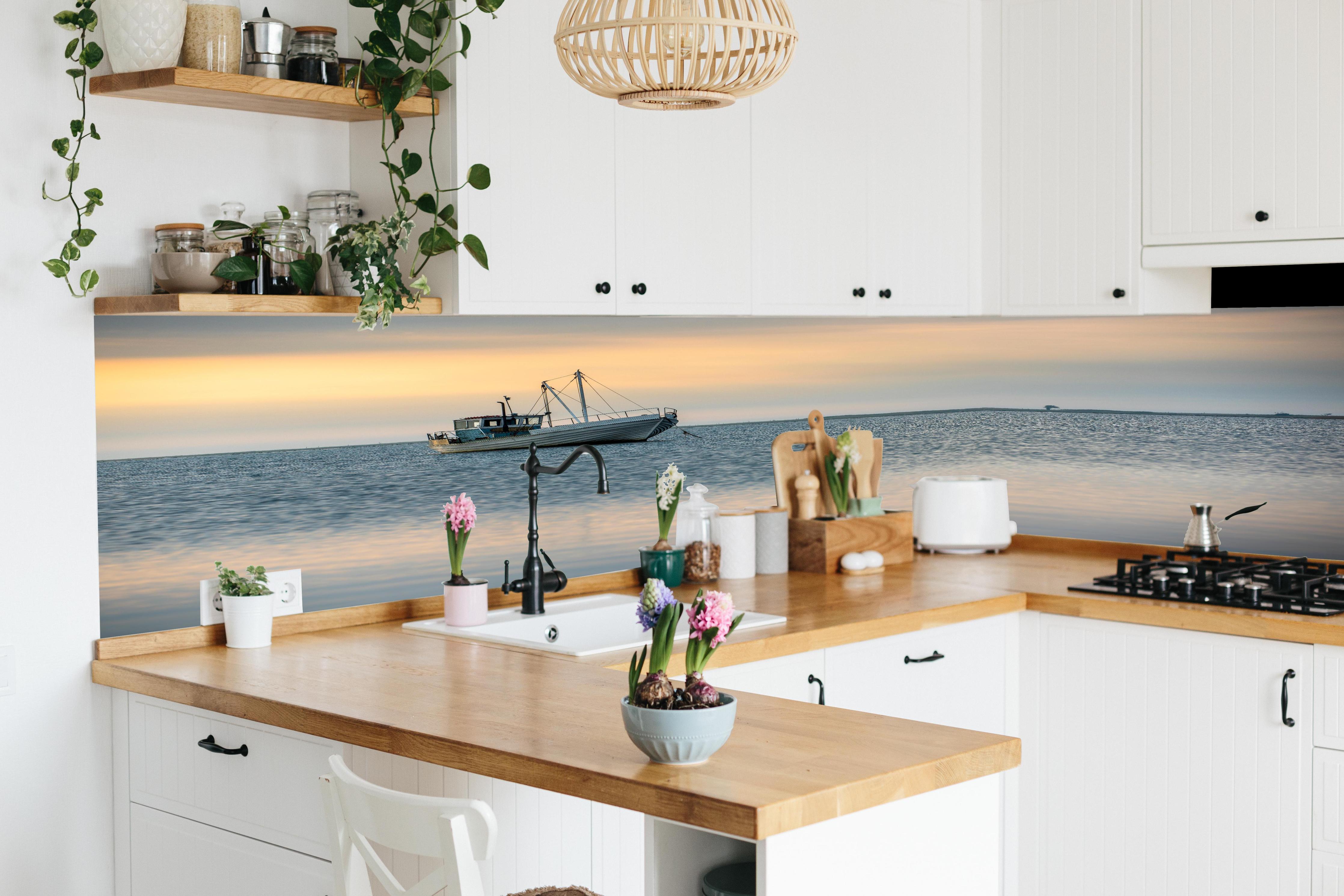 Küche - Idyllisches Boot auf ruhigem Wasser bei Sonnenuntergang hinter weißen Hochglanz-Küchenregalen und schwarzem Wasserhahn