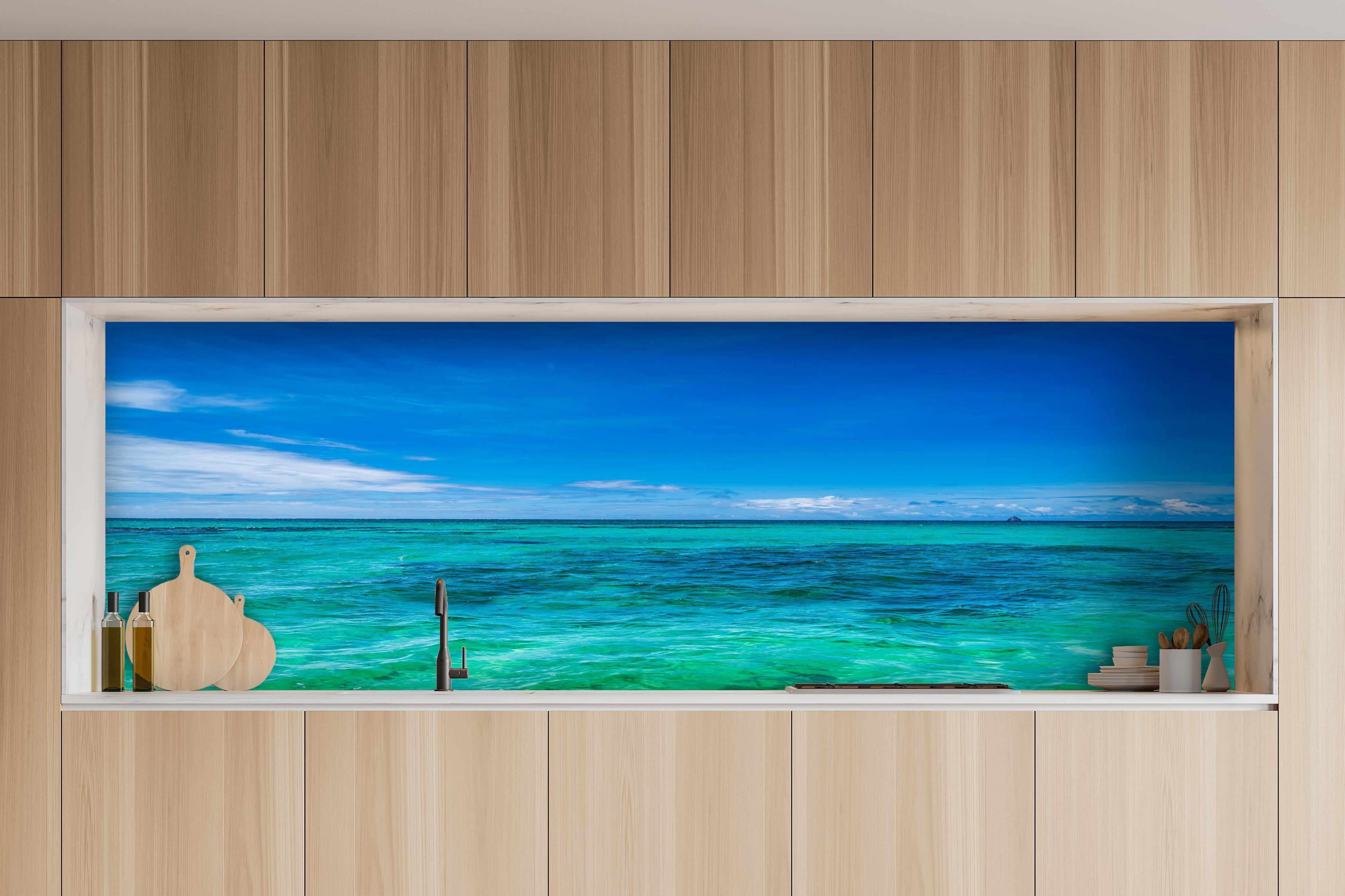 Küche - Klarmarkiertes, türkisblaues Wasser unter hellem Himmel hinter weißen Hochglanz-Küchenregalen und schwarzem Wasserhahn