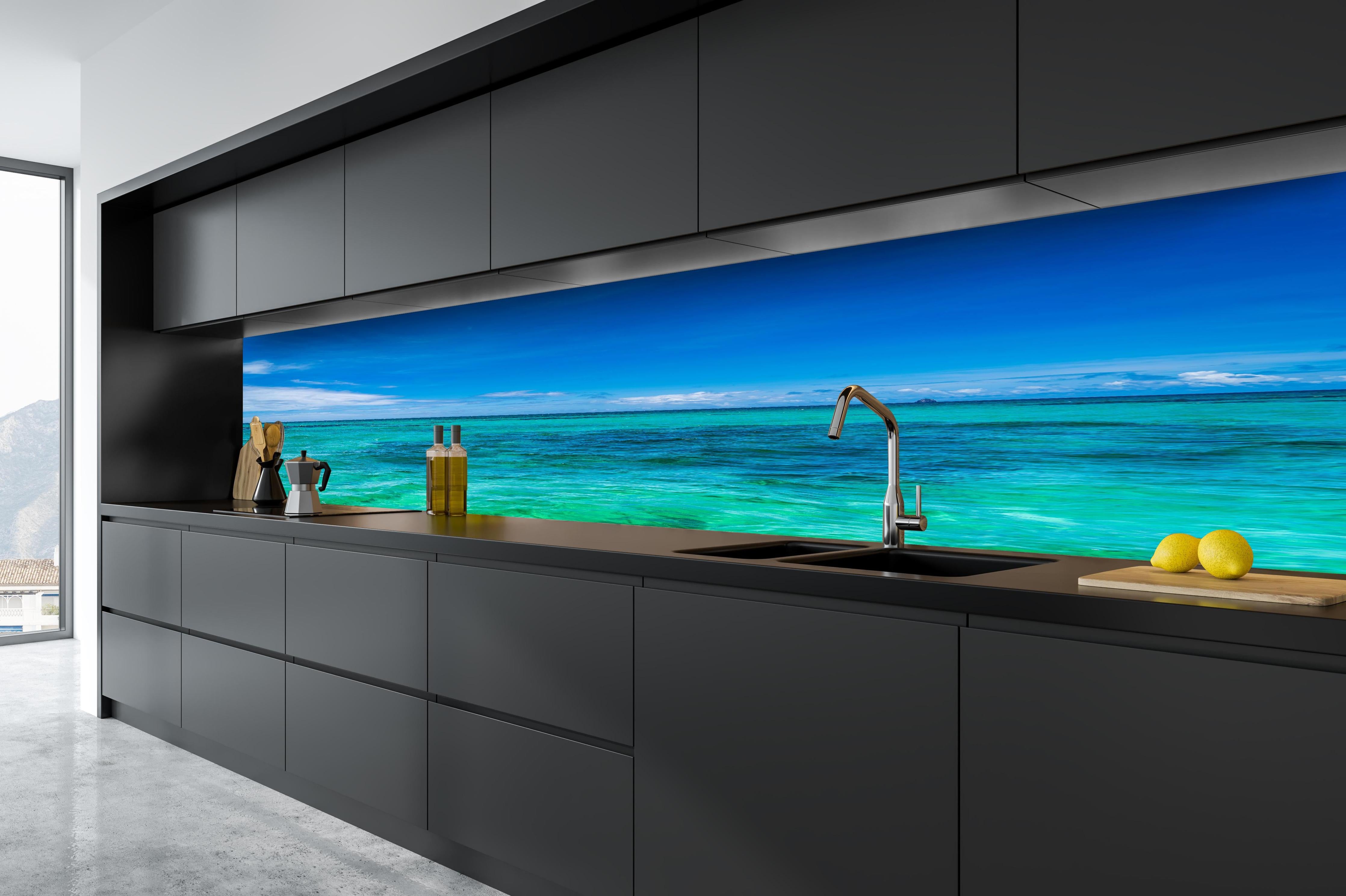 Küche - Klarmarkiertes, türkisblaues Wasser unter hellem Himmel hinter weißen Hochglanz-Küchenregalen und schwarzem Wasserhahn
