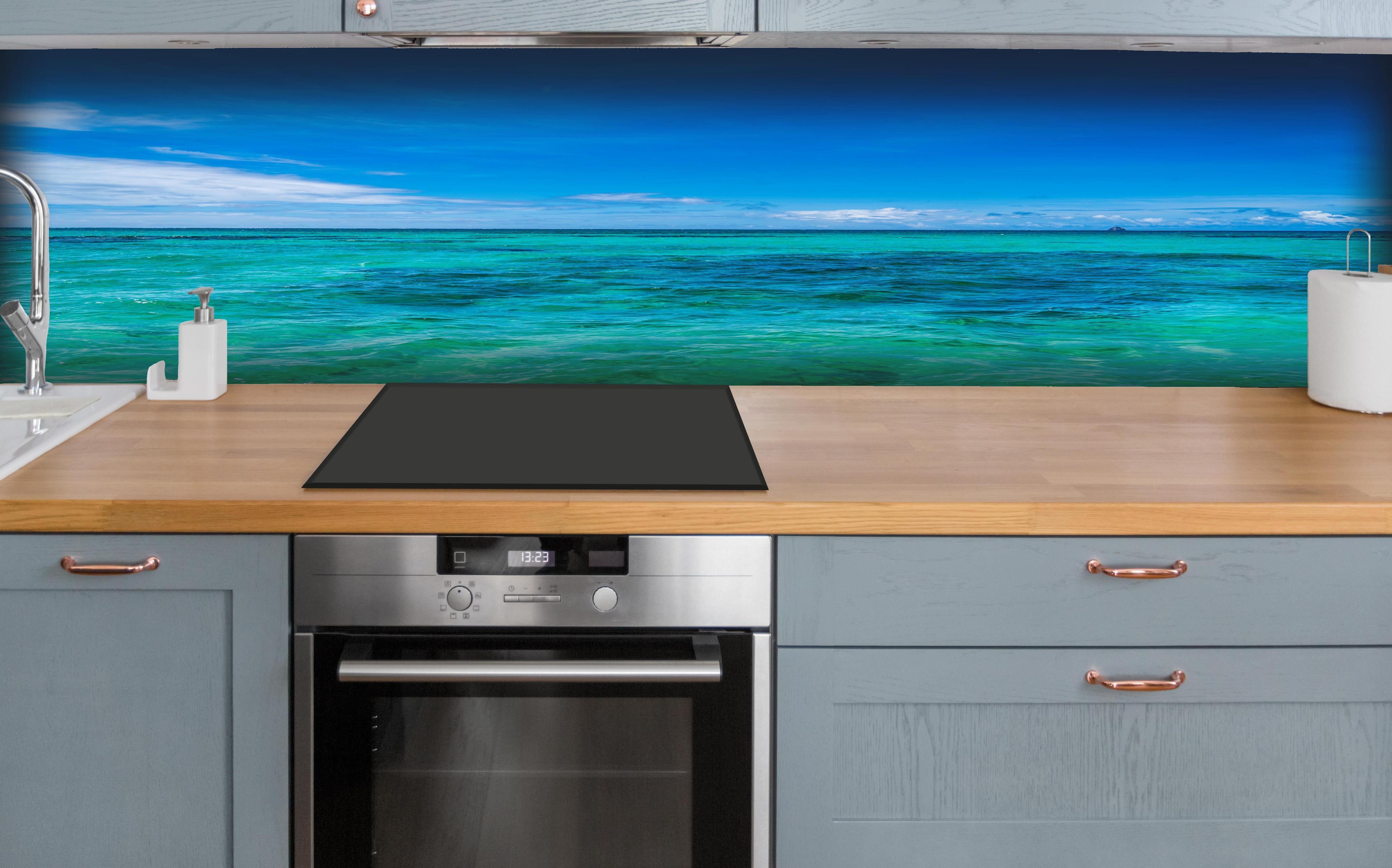 Küche - Klarmarkiertes, türkisblaues Wasser unter hellem Himmel hinter weißen Hochglanz-Küchenregalen und schwarzem Wasserhahn