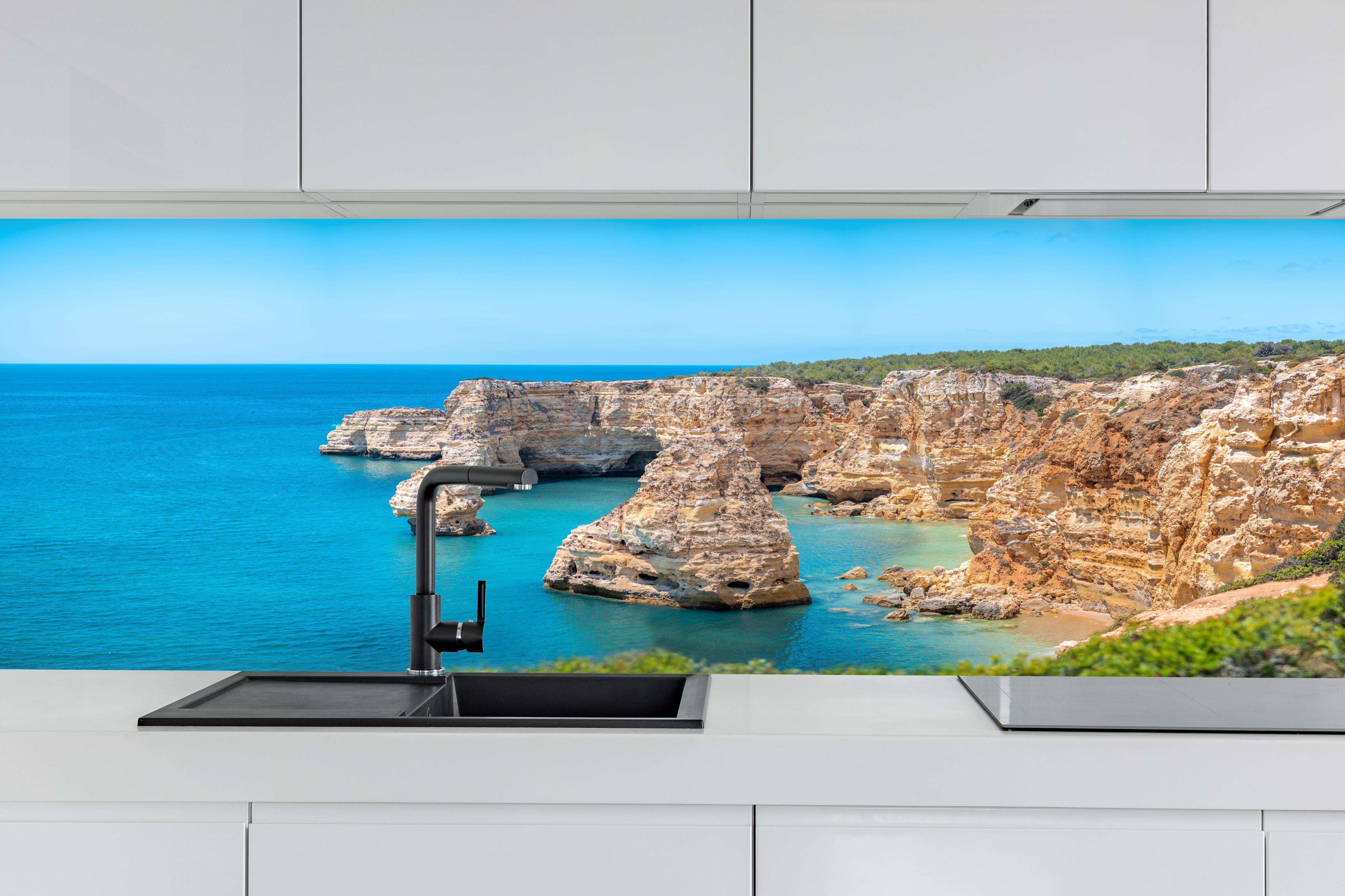 Küche - Algarve-Klippen am türkisblauen Meer hinter weißen Hochglanz-Küchenregalen und schwarzem Wasserhahn