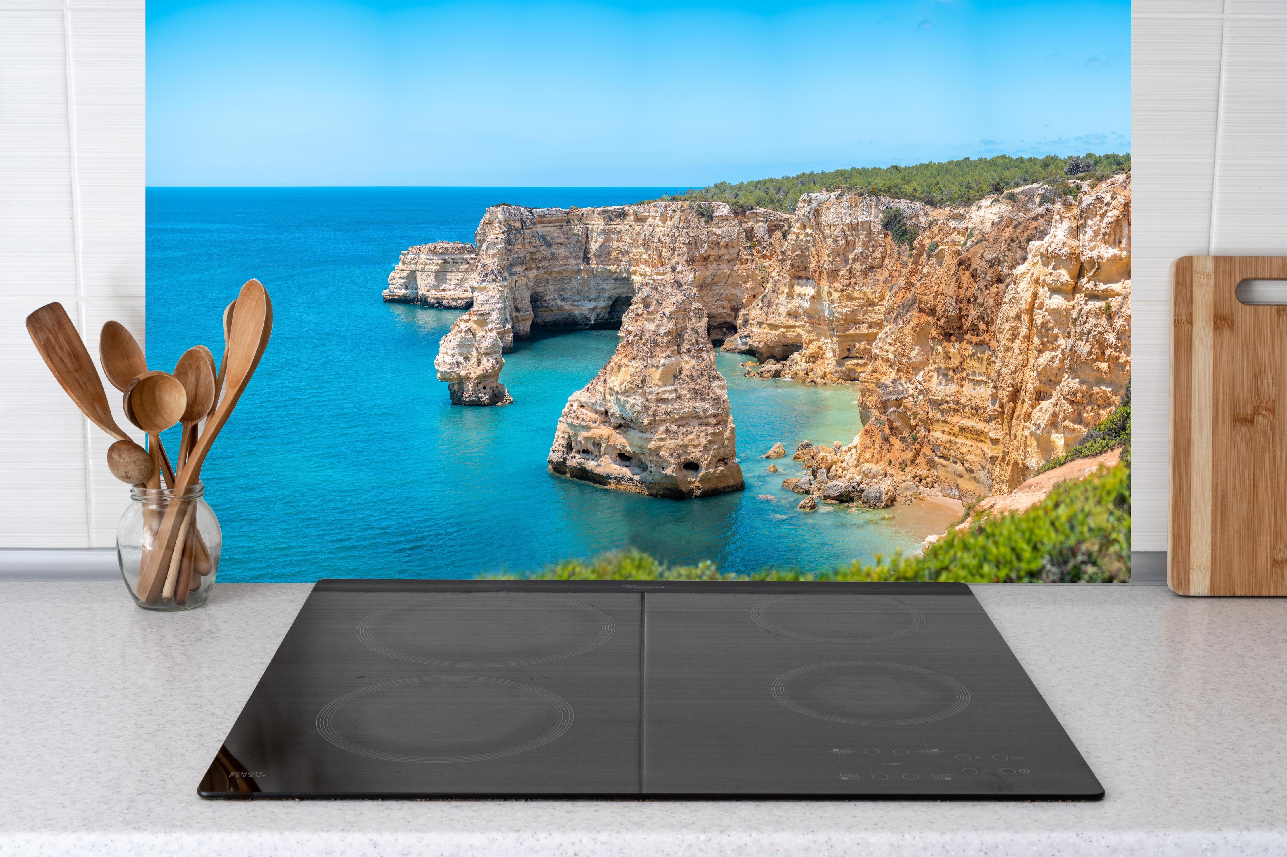 Küche - Algarve-Klippen am türkisblauen Meer hinter Cerankochfeld und Holz-Kochutensilien