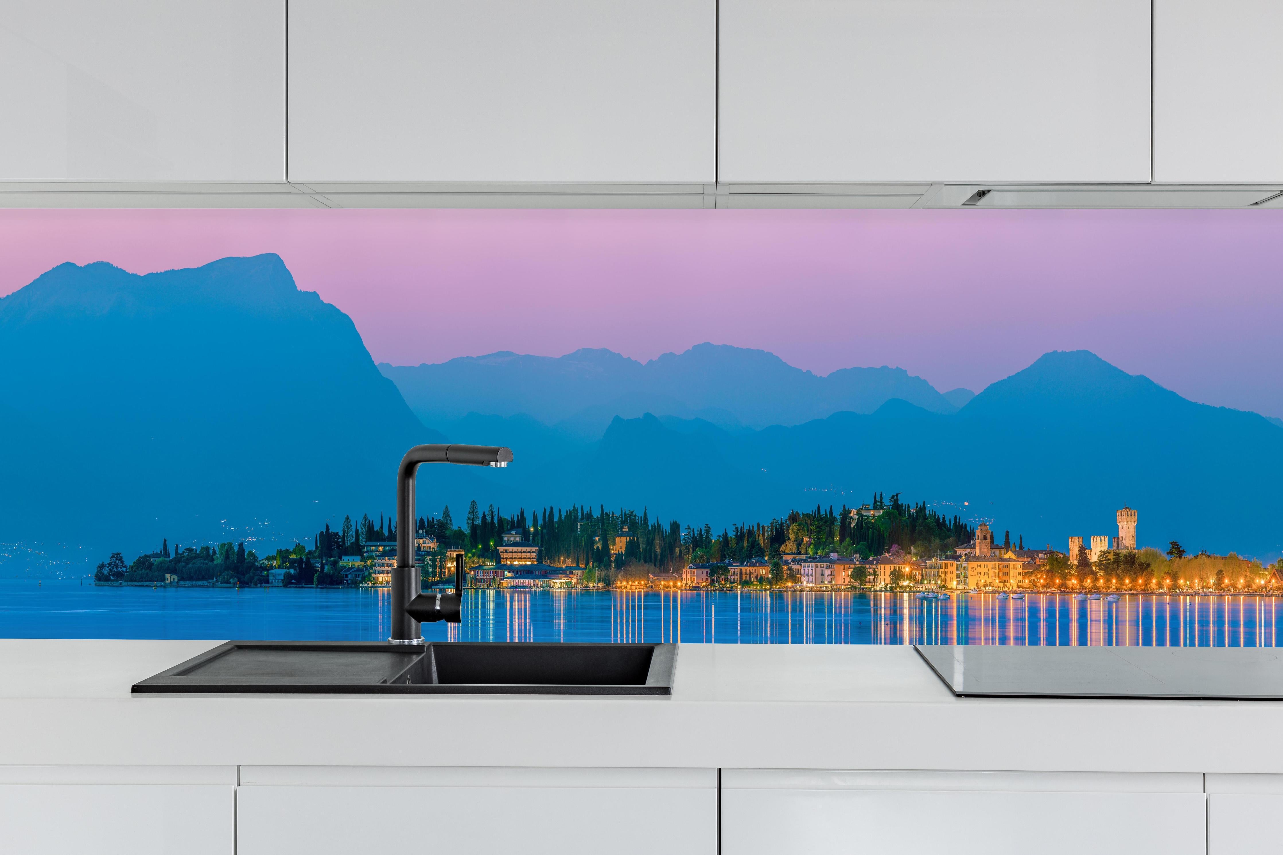 Küche - Gardasee Abenddämmerung Panorama hinter weißen Hochglanz-Küchenregalen und schwarzem Wasserhahn