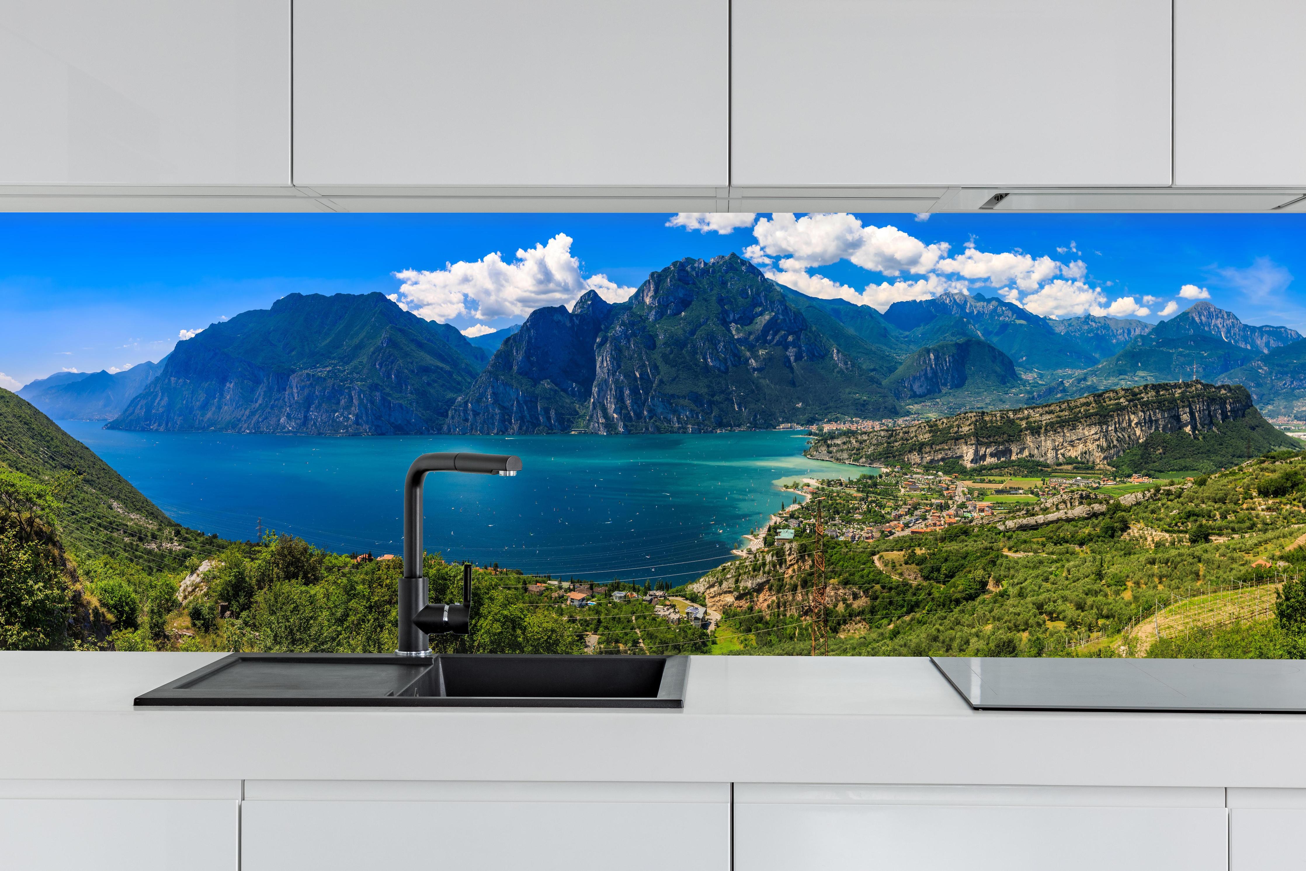 Küche - Gardasee Panorama in Blau und Grün hinter weißen Hochglanz-Küchenregalen und schwarzem Wasserhahn