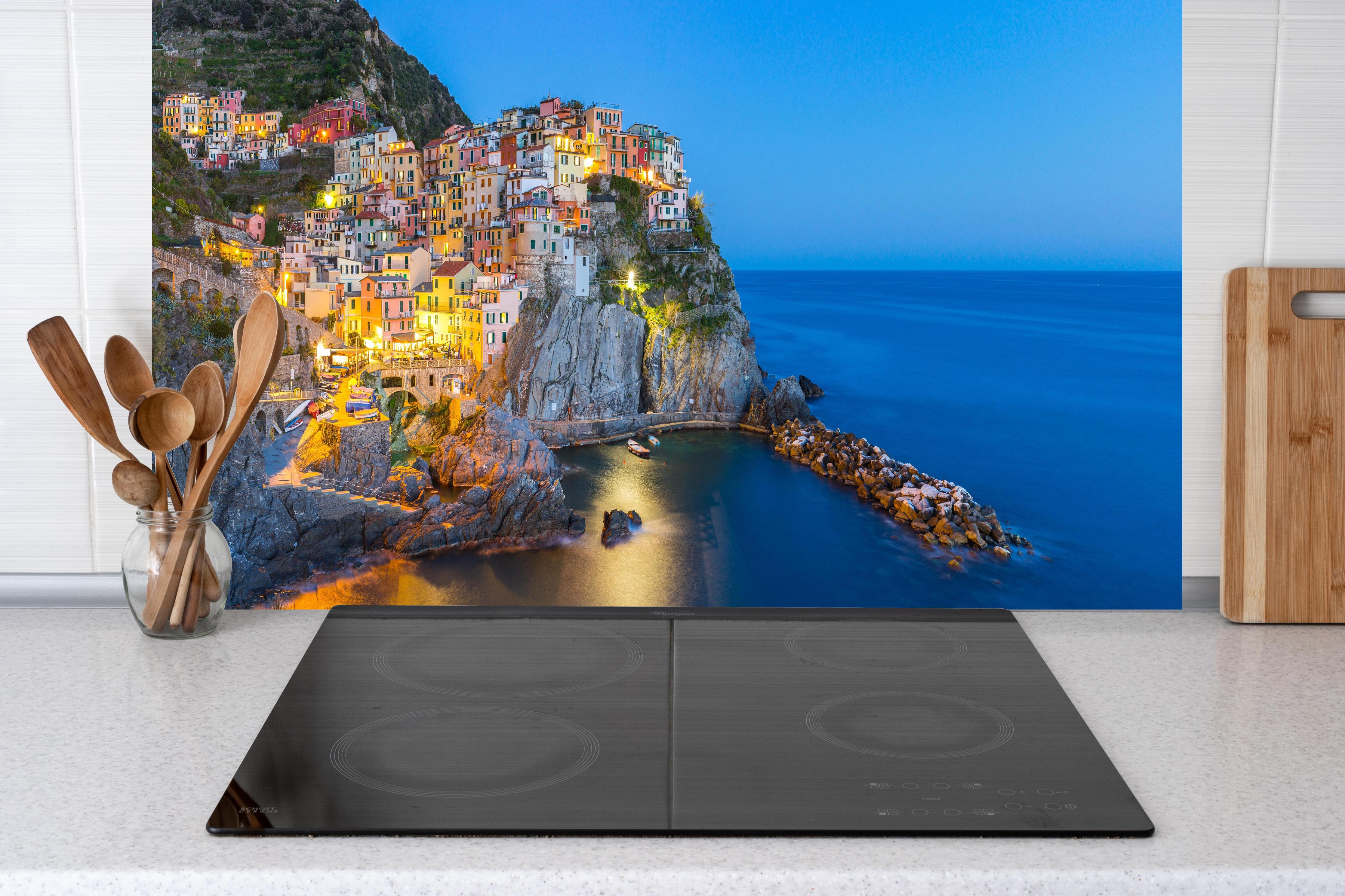 Küche - Italienische Küstenstadt bei Abendlicht hinter Cerankochfeld und Holz-Kochutensilien