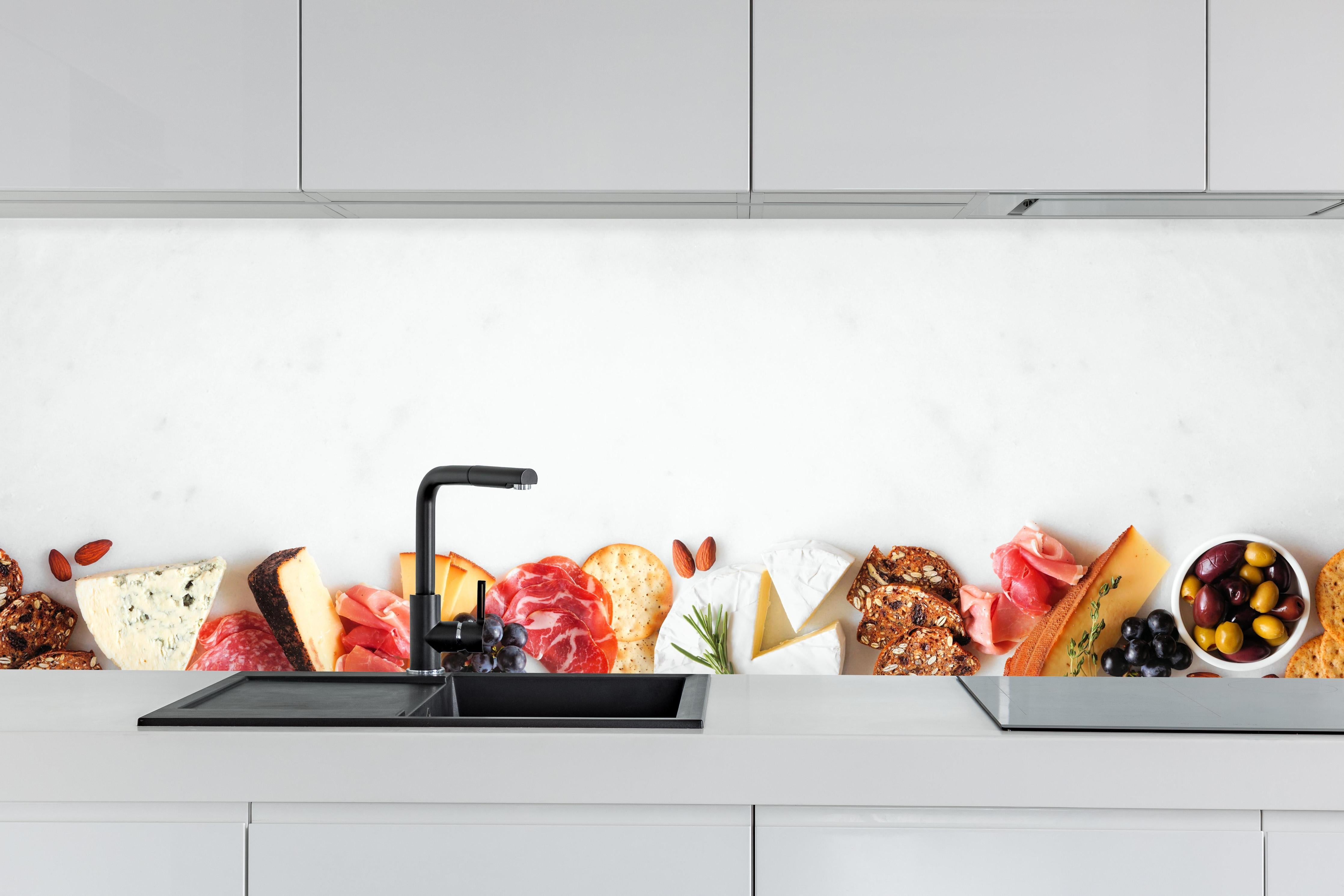 Küche - Käse und Antipasti auf Weiß hinter weißen Hochglanz-Küchenregalen und schwarzem Wasserhahn