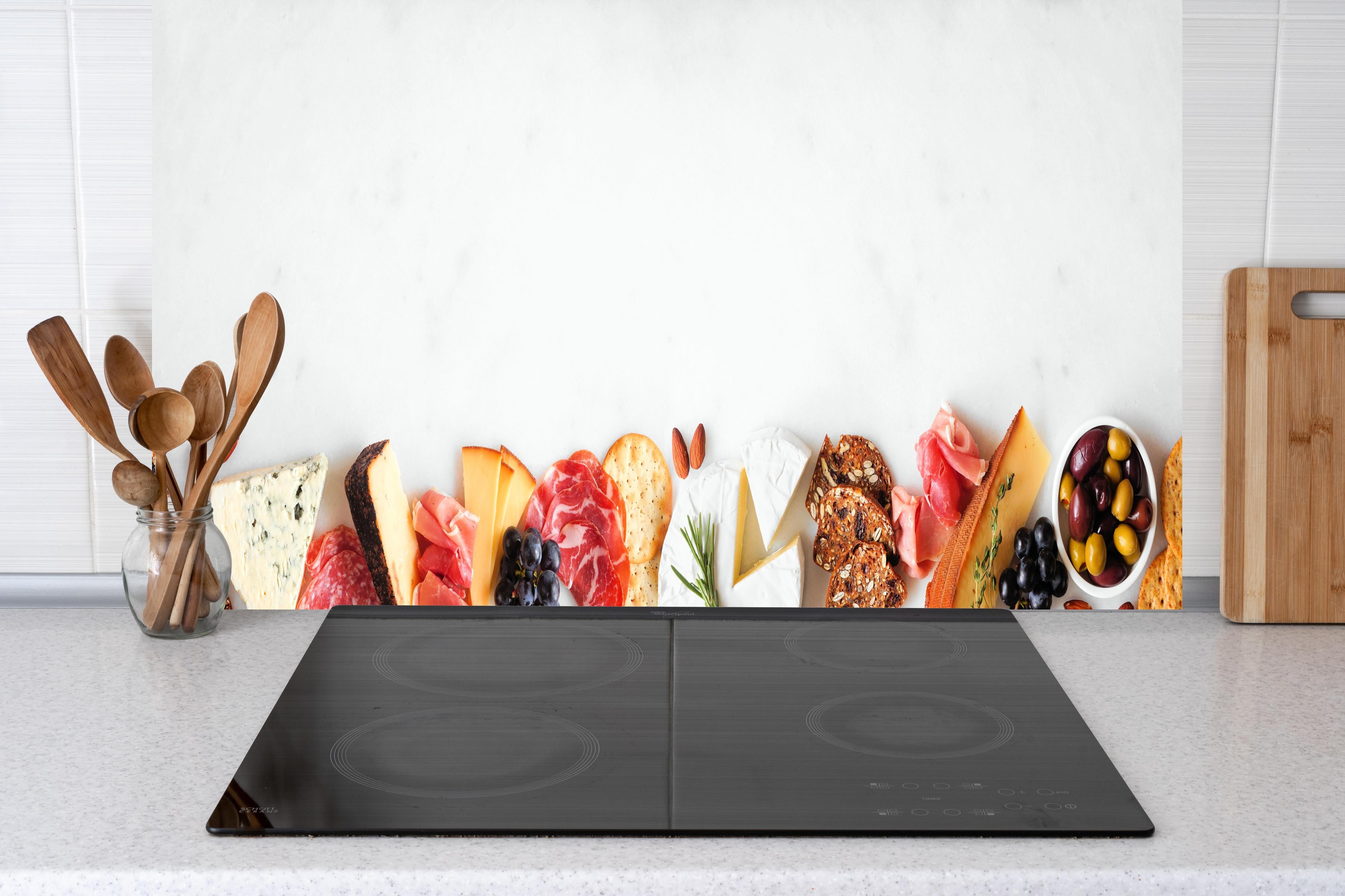 Küche - Käse und Antipasti auf Weiß hinter Cerankochfeld und Holz-Kochutensilien