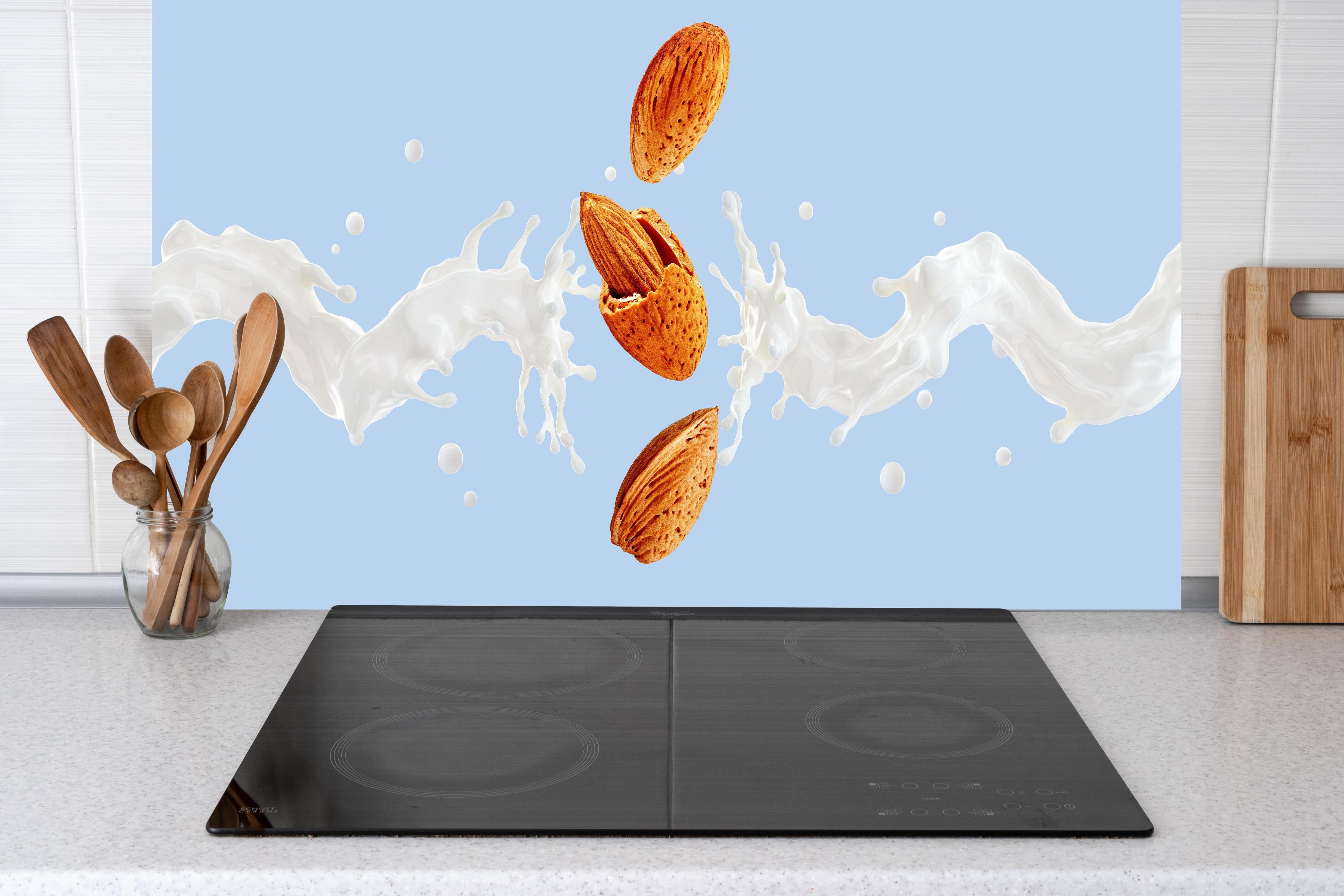 Küche - Mandelmilch-Splash auf Blau hinter Cerankochfeld und Holz-Kochutensilien