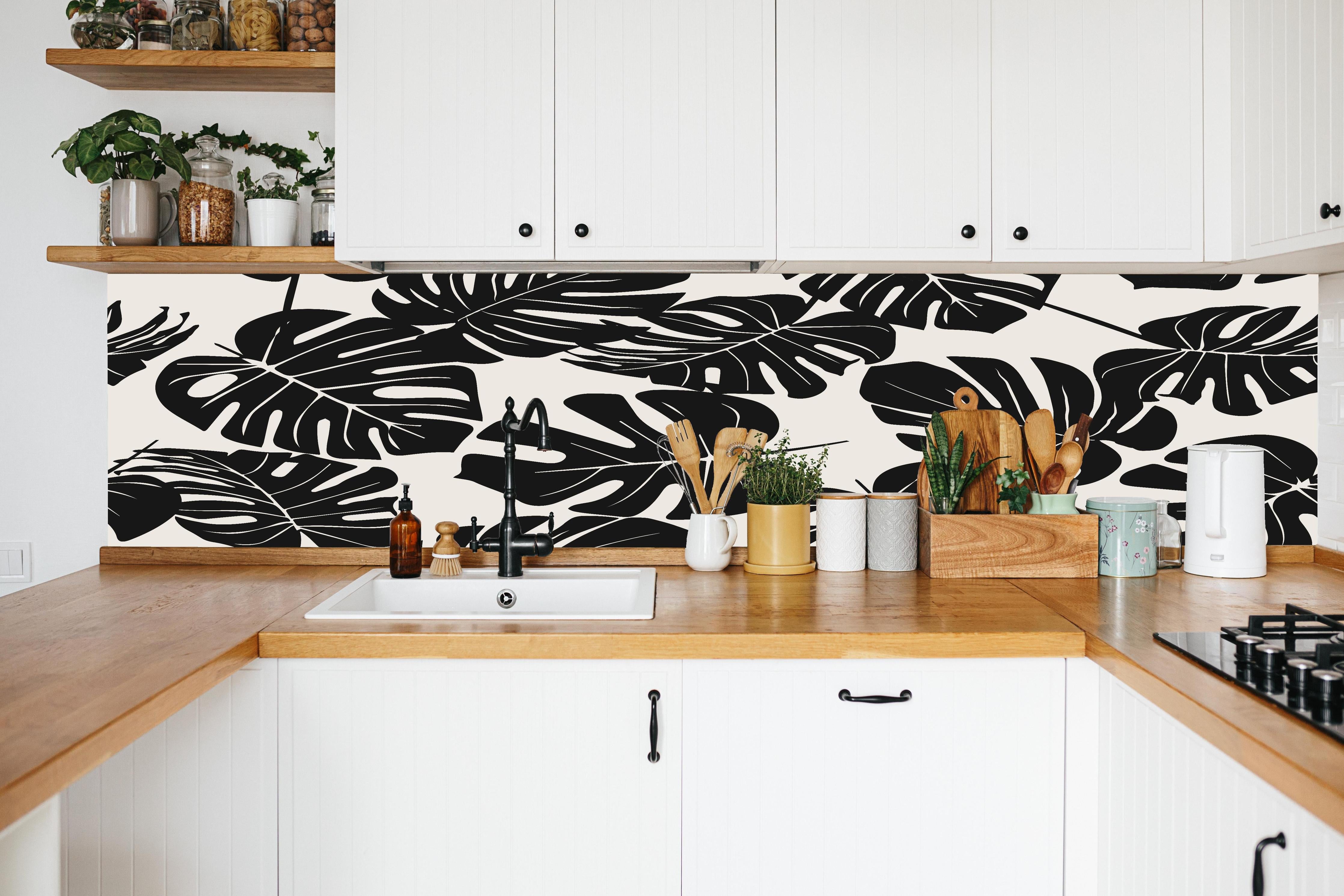 Küche - Monstera Schwarz-Beige Muster in weißer Küche hinter Gewürzen und Kochlöffeln aus Holz