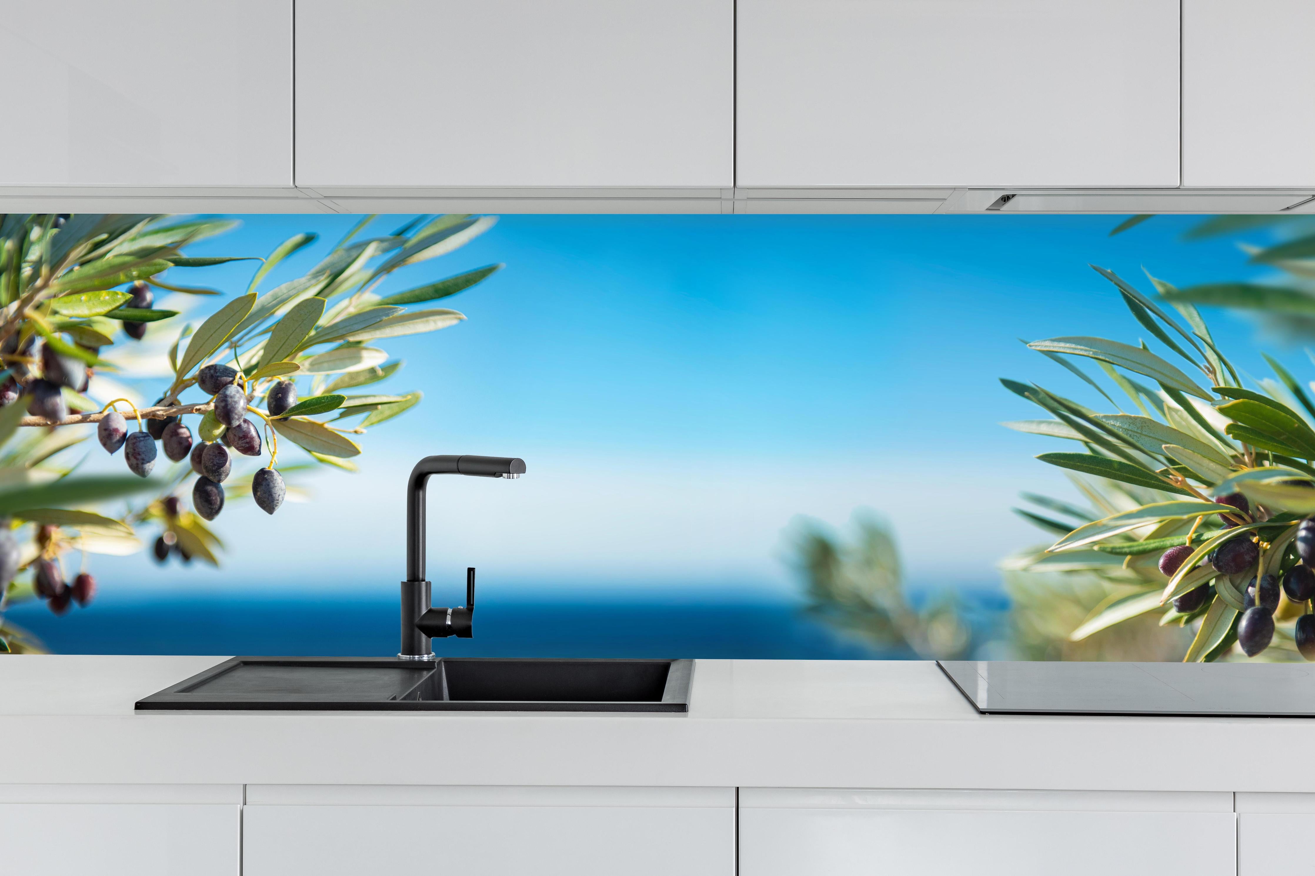 Küche - Olivenzweig am Meer Blau-Grün hinter weißen Hochglanz-Küchenregalen und schwarzem Wasserhahn